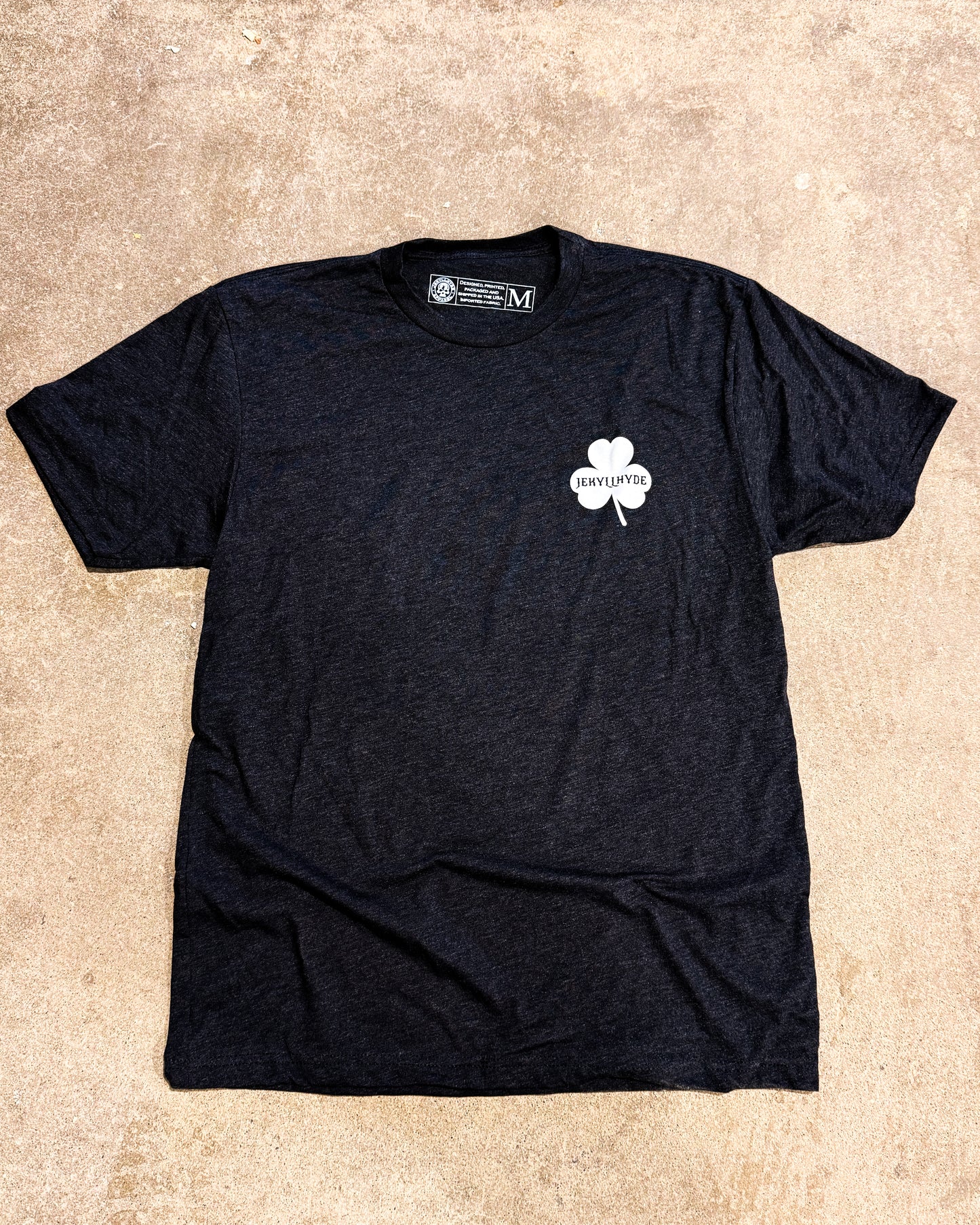 Black tshirt with a shamrock on concrete. 