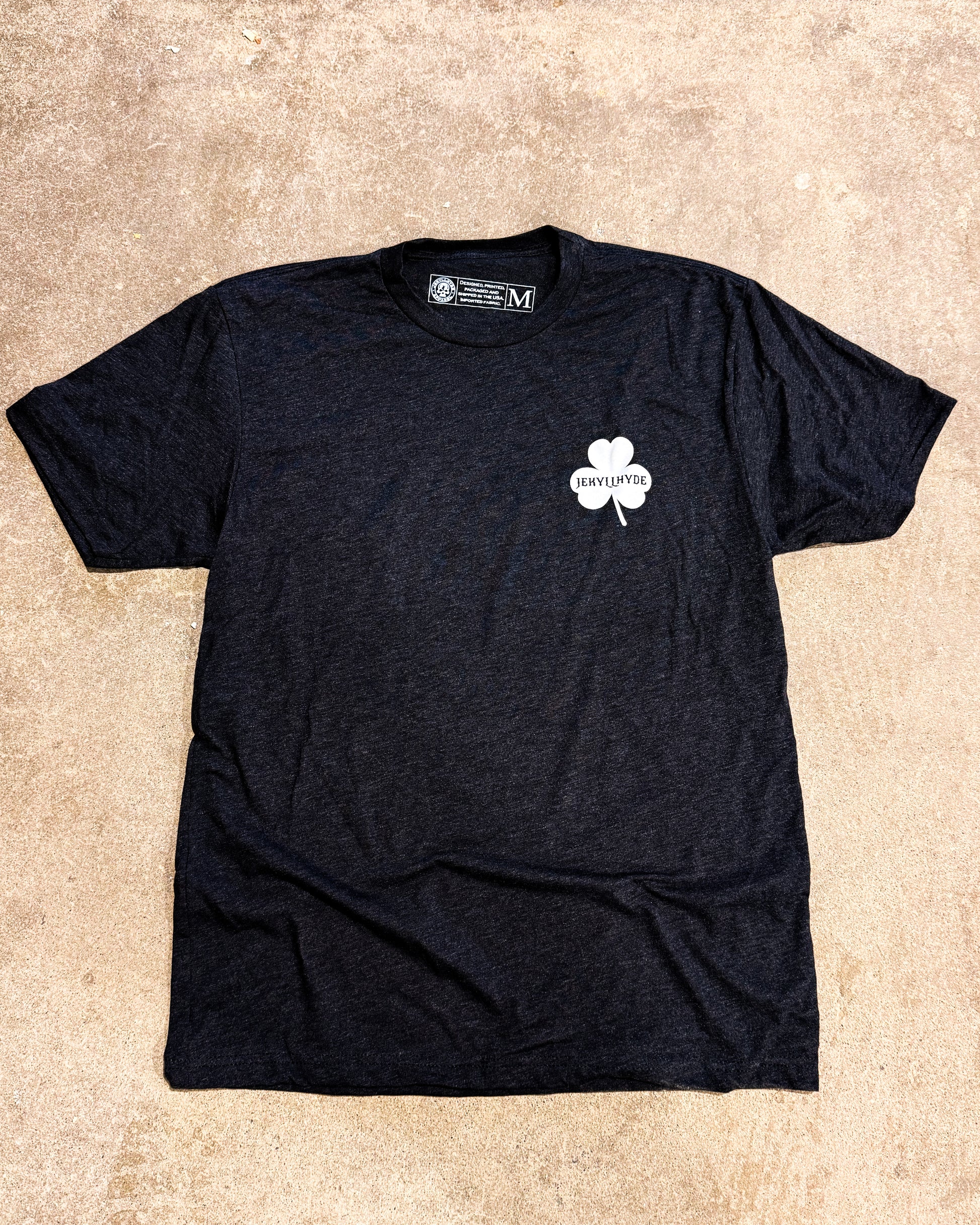 Black tshirt with a shamrock on concrete. 