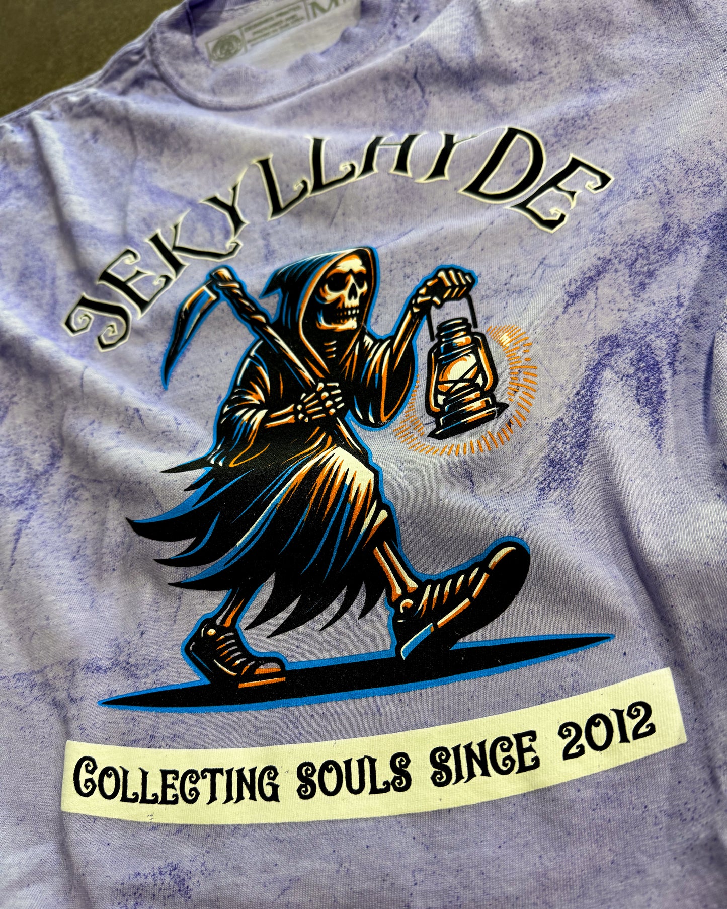 T-shirt with a graphic of a skeleton holding a lantern and text 'Jekyll & Hyde Collecting Souls Since 2012' on a purple background.