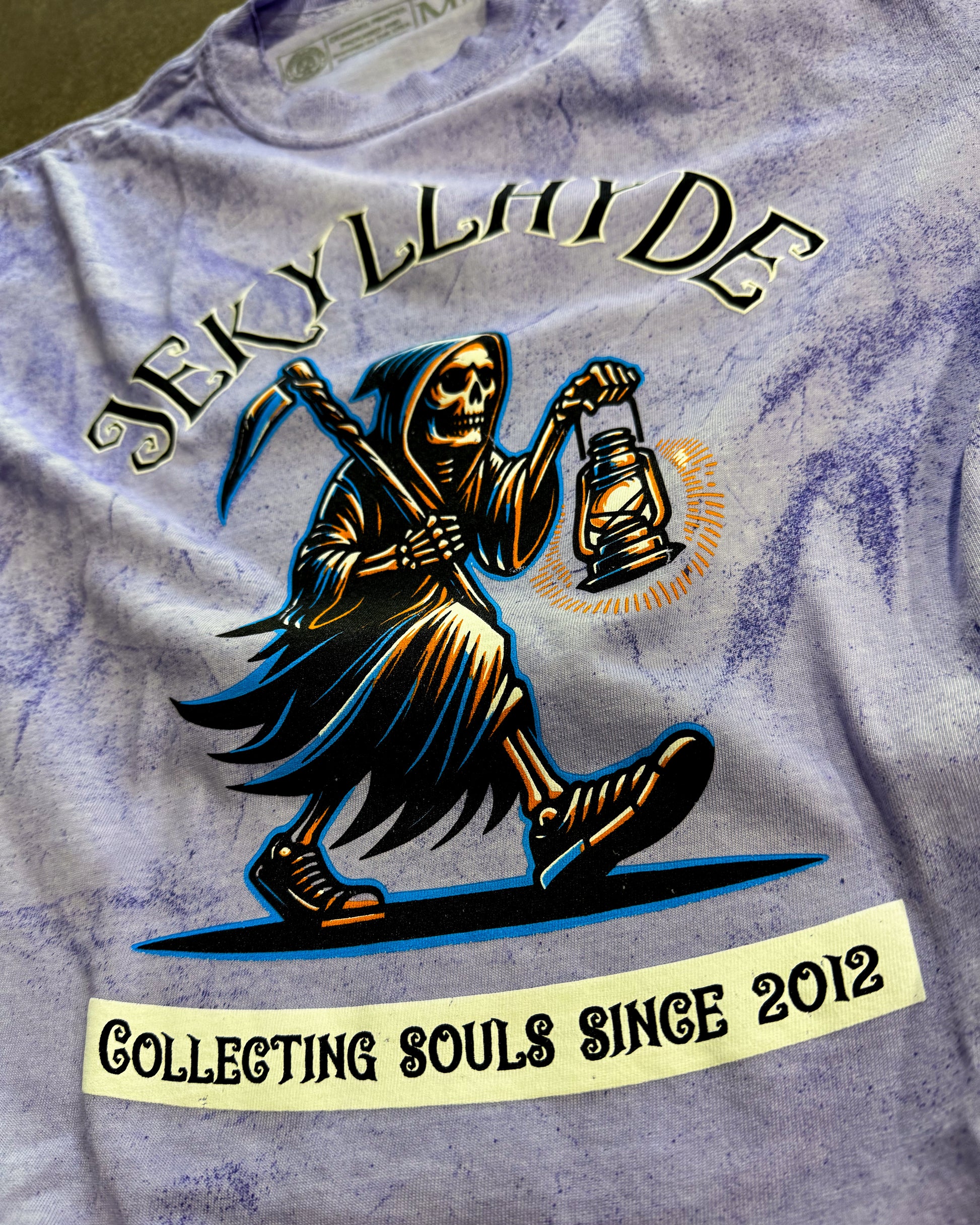 T-shirt with a graphic of a skeleton holding a lantern and text 'Jekyll & Hyde Collecting Souls Since 2012' on a purple background.