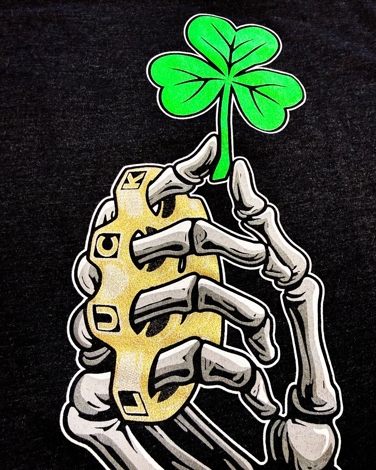 Skeleton hand holding a gold coin with a green four-leaf clover on a black background