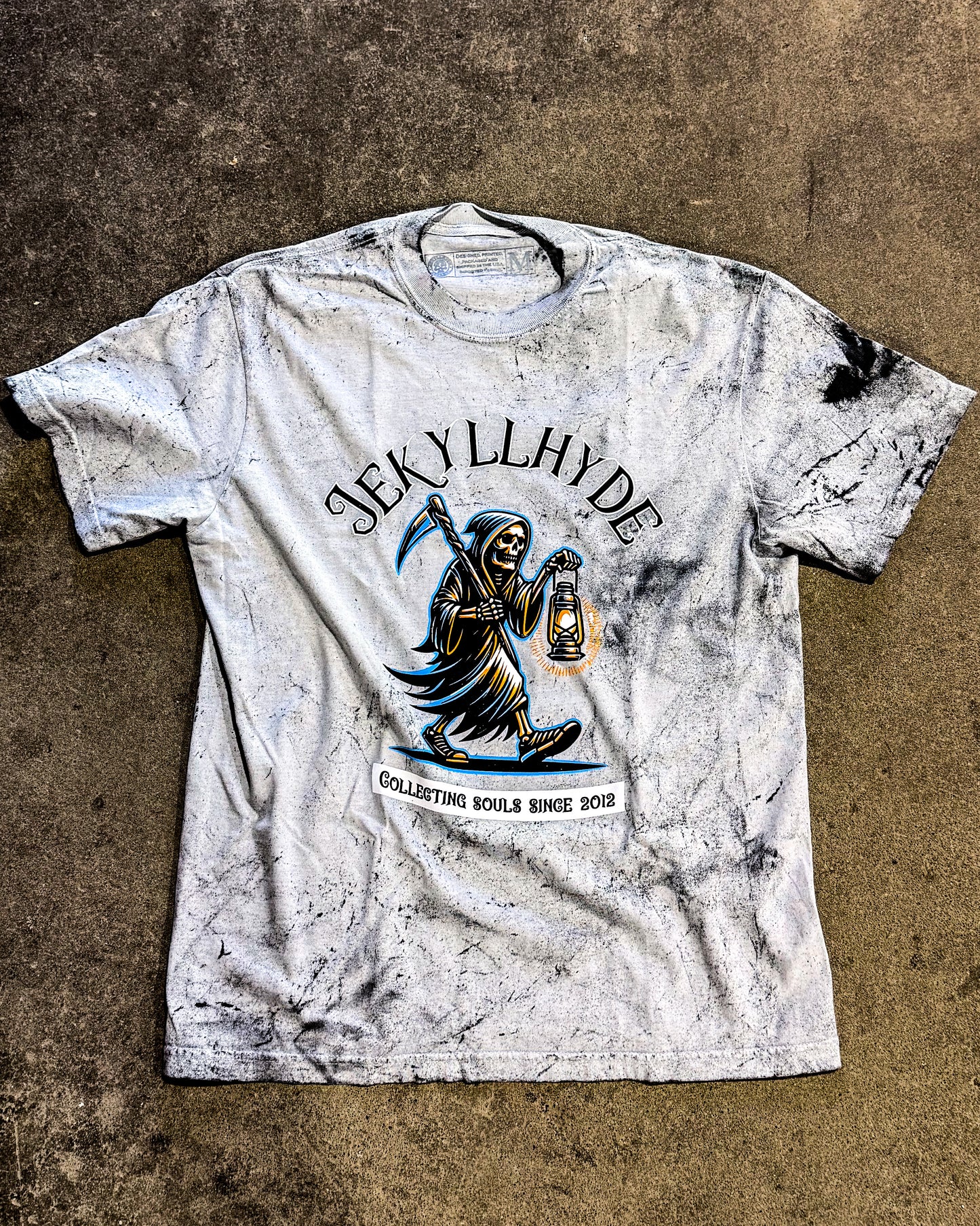 White marbly t-shirt with black and blue graphic design on a textured brown surface