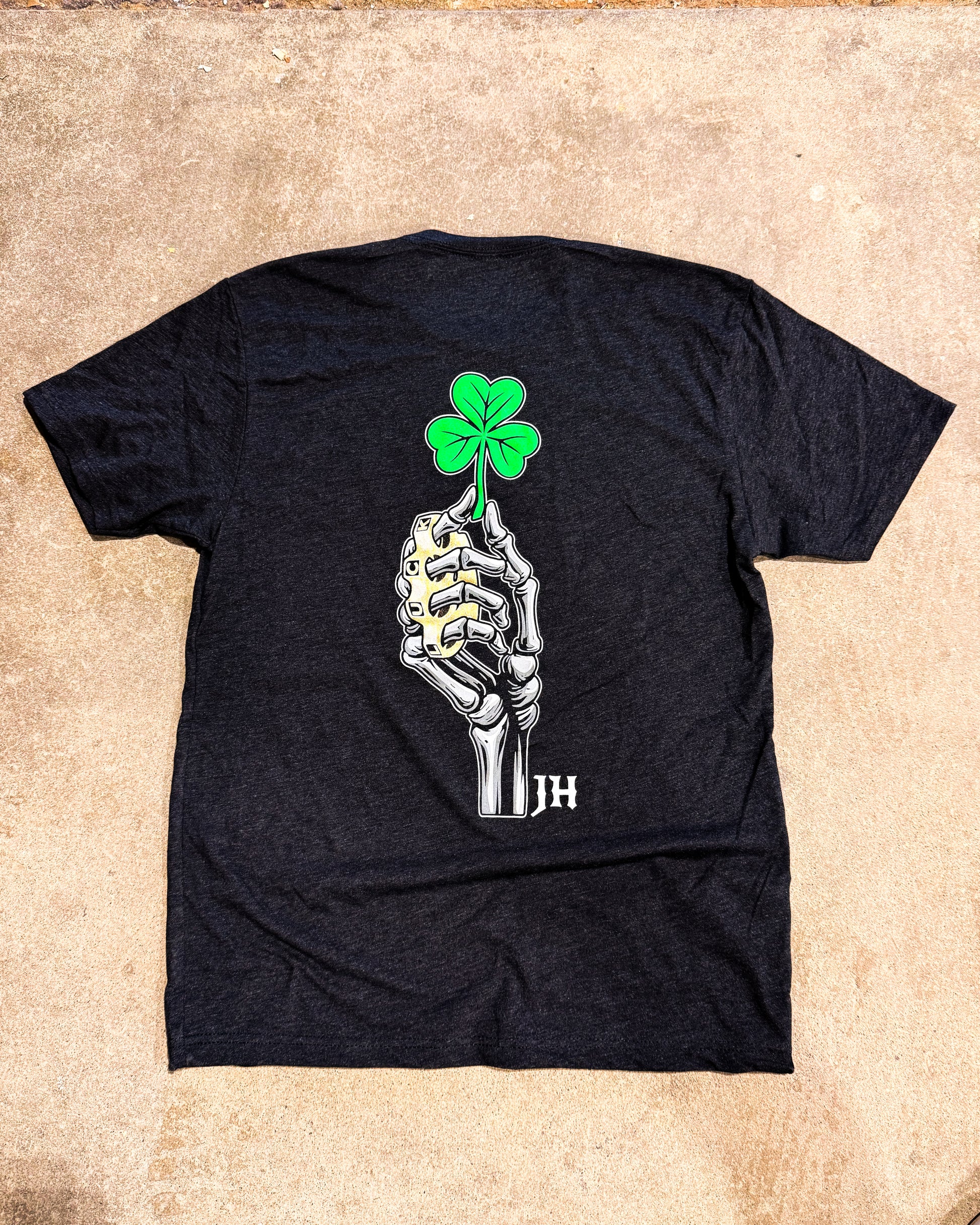 Black t-shirt with a skeleton hand holding a four-leaf clover design on a beige surface