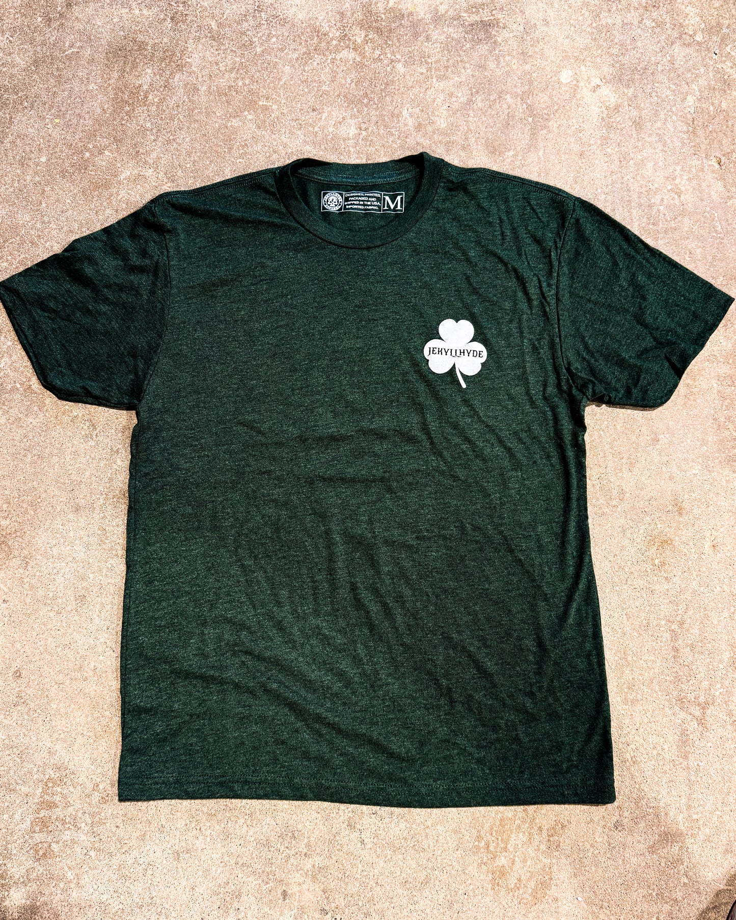 Green t-shirt with a white shamrock logo on a beige surface