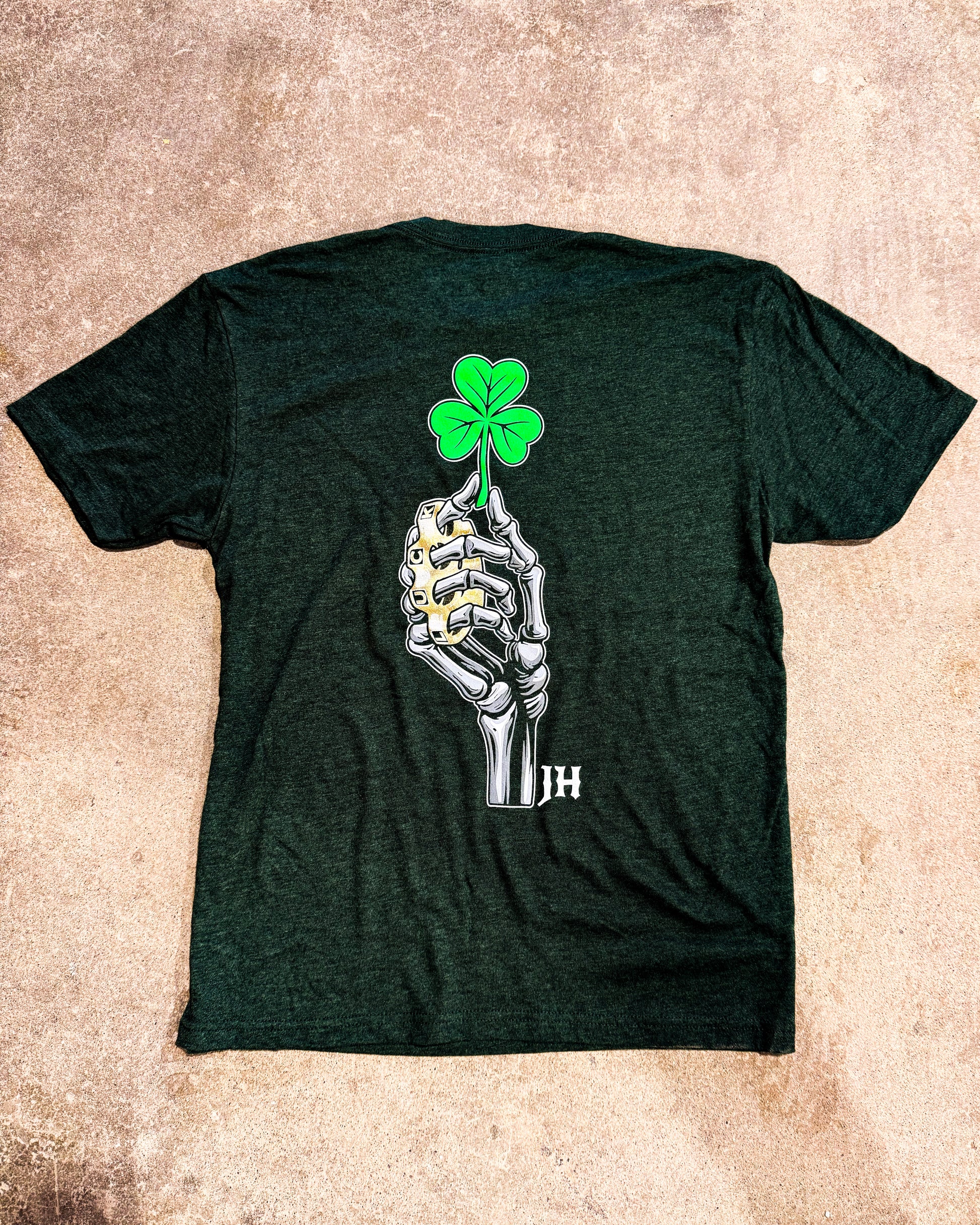 Green t-shirt with a skeleton hand holding a four-leaf clover design on a beige surface