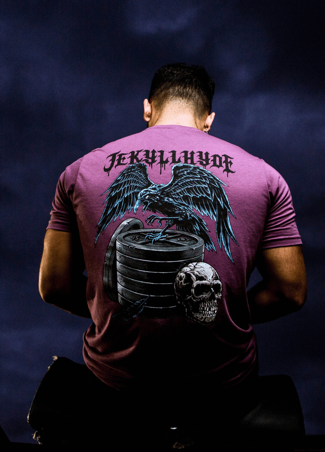 Man sitting with his back to the camera wearing a purple Raven and skull tshirt. 