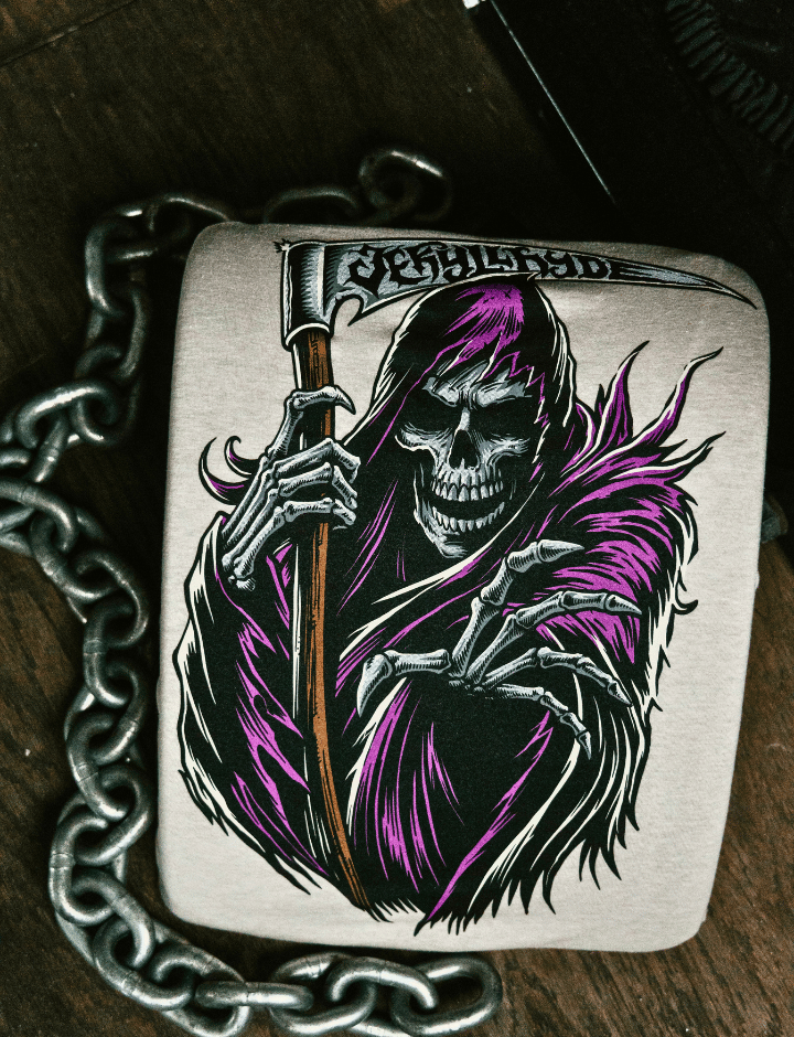 A sand colored shirt with a grim reaper on it laying on a wooden background with chains.