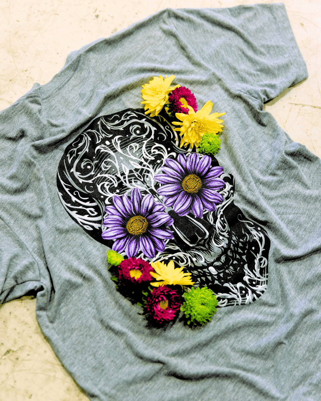 Grey shirt on the floor with a sugar skull design with flower eyes. 