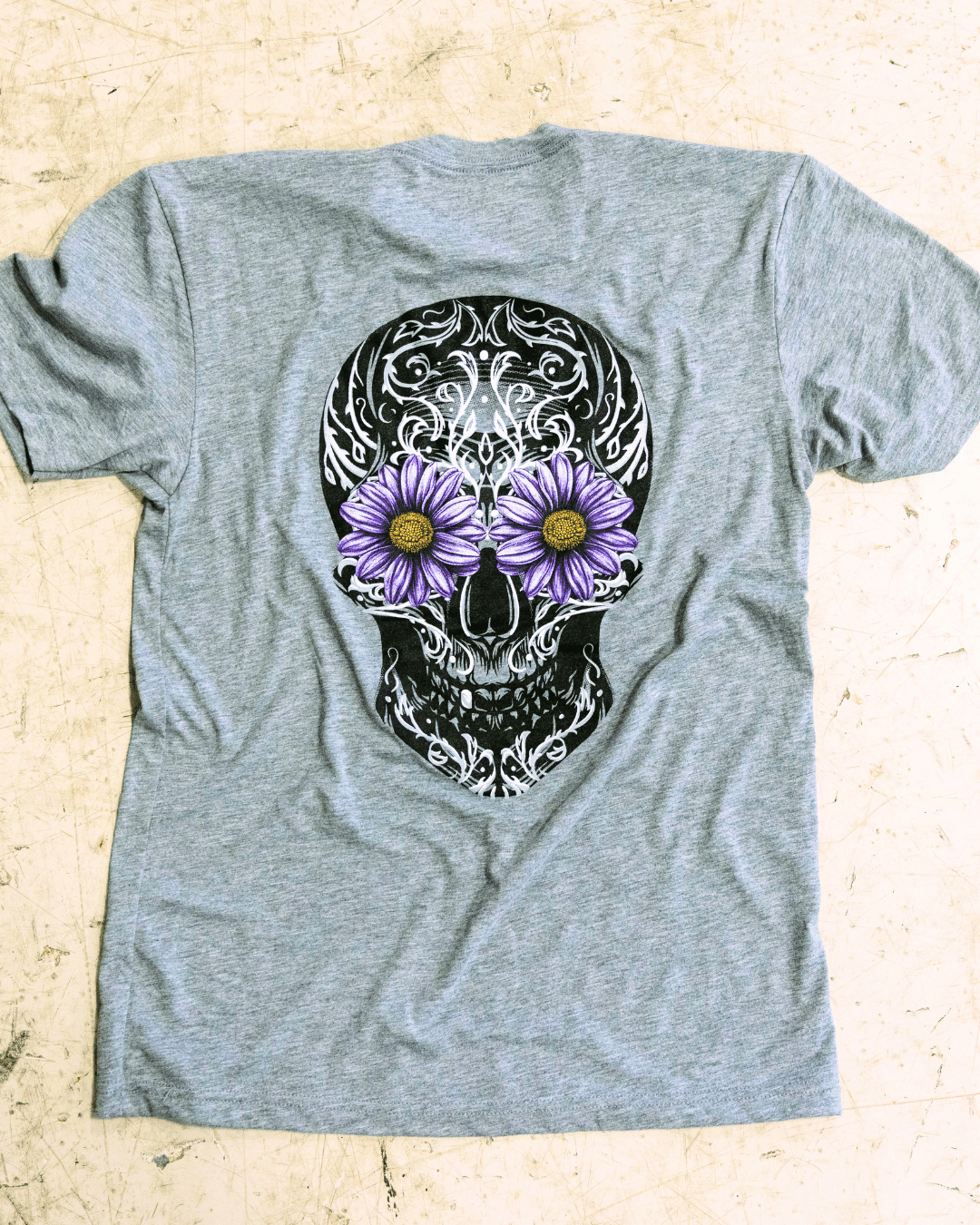 Grey tshirt with a sugar skull design with flower eye on the floor. 