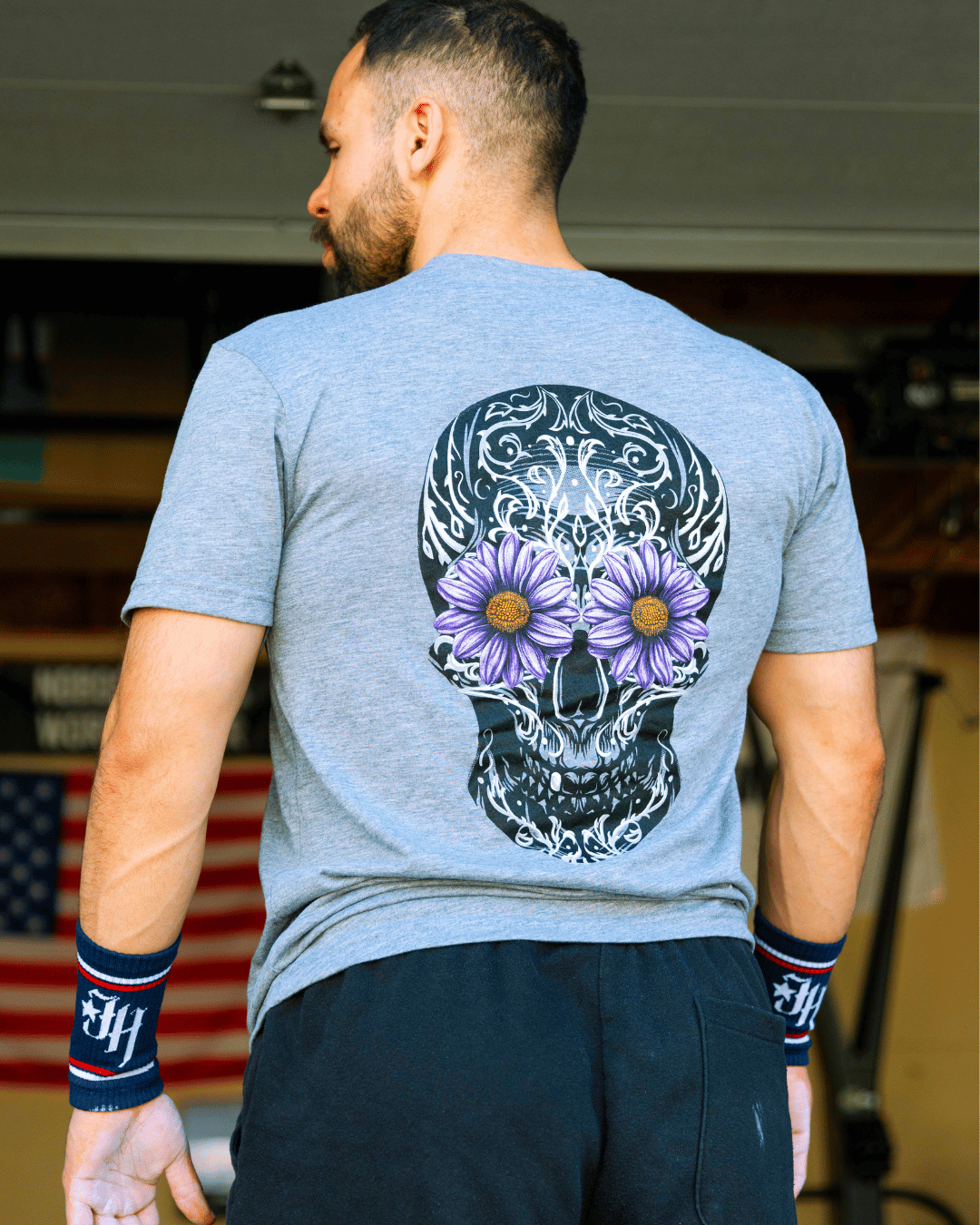 Man standing with back to the camera wearing a grey shirt with a sugar skull on it. 