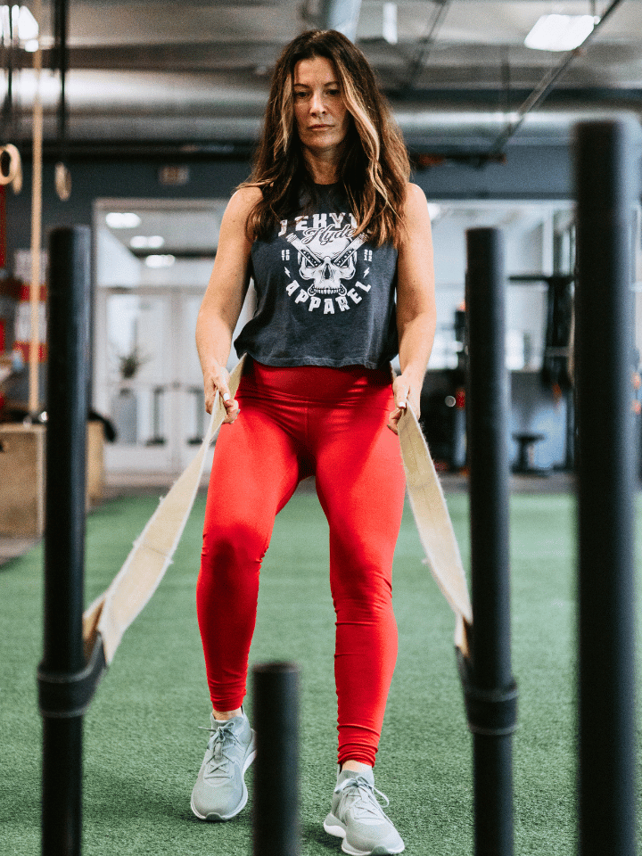 Woman pulling a sled on turf wearing a blue crop tank with a skull on it. 