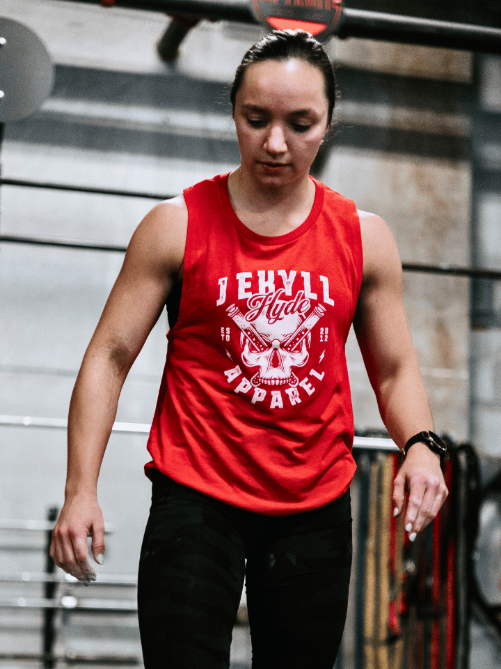 Woman looking at the ground wearing a red muscle tank with a skull on it. 