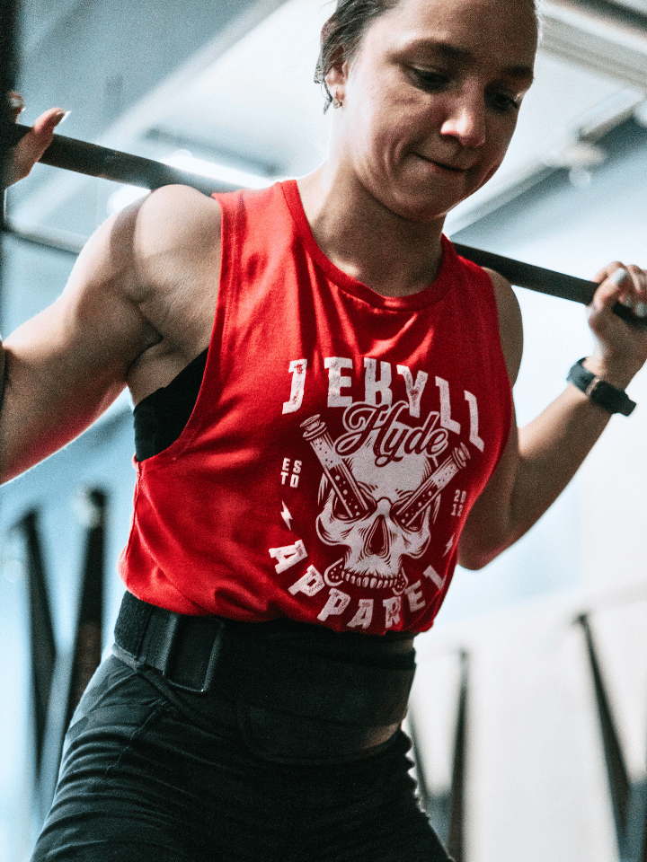 Woman squatting wearing a red muscle tank with a skull on it. 