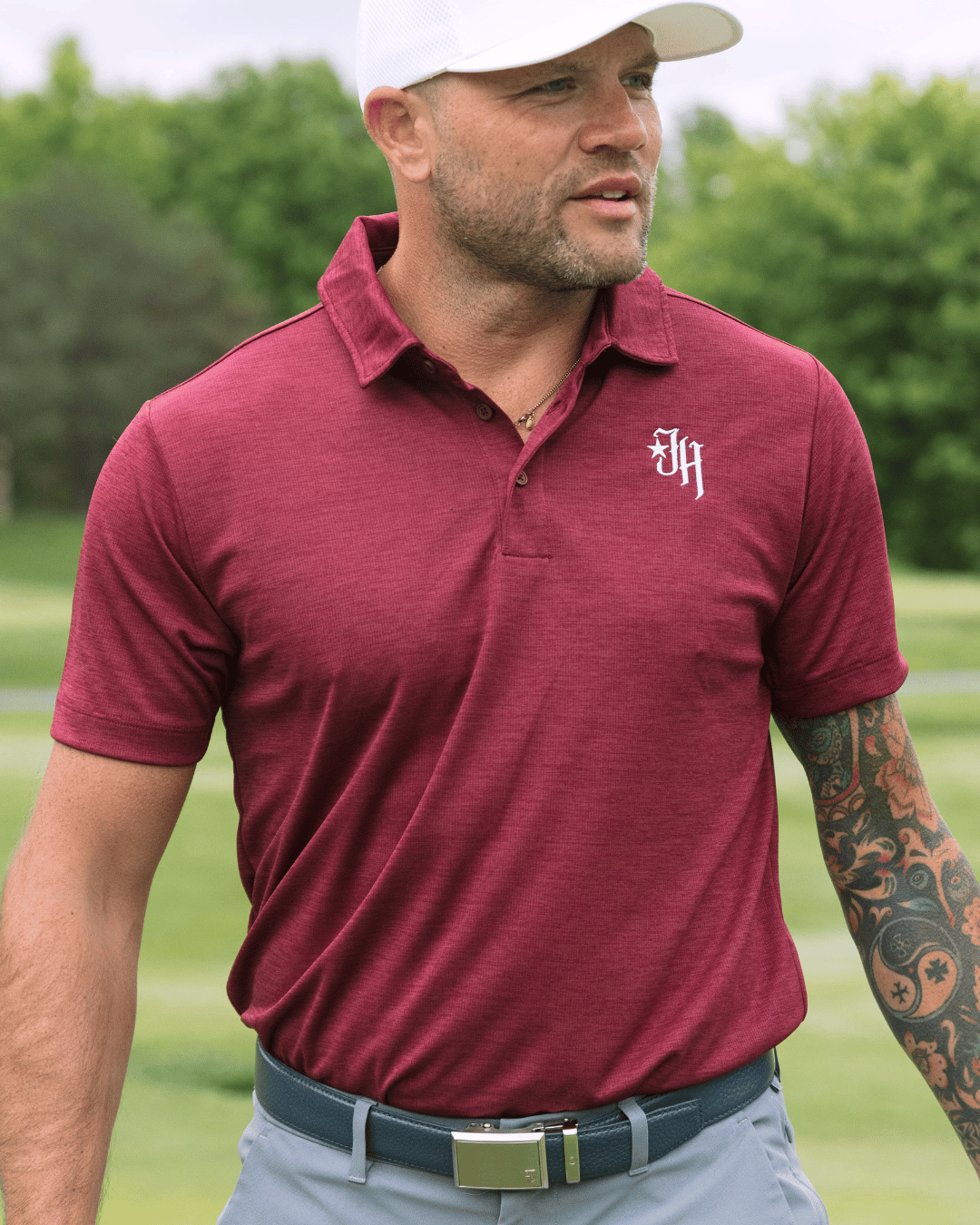 Man wearing a maroon polo shirt with a logo on a golf course