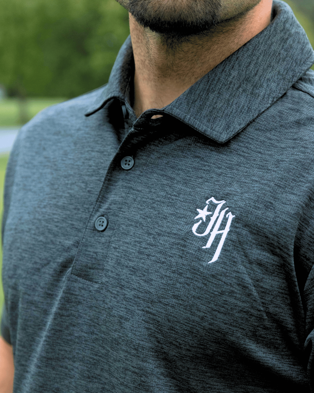 Gray polo shirt with a logo on the chest worn by a person outdoors.