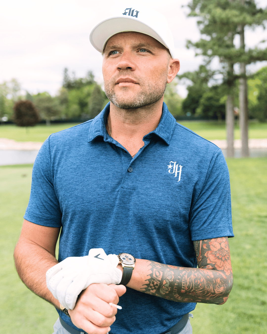 Man in a blue polo shirt with a logo, holding a golf club on a golf course.