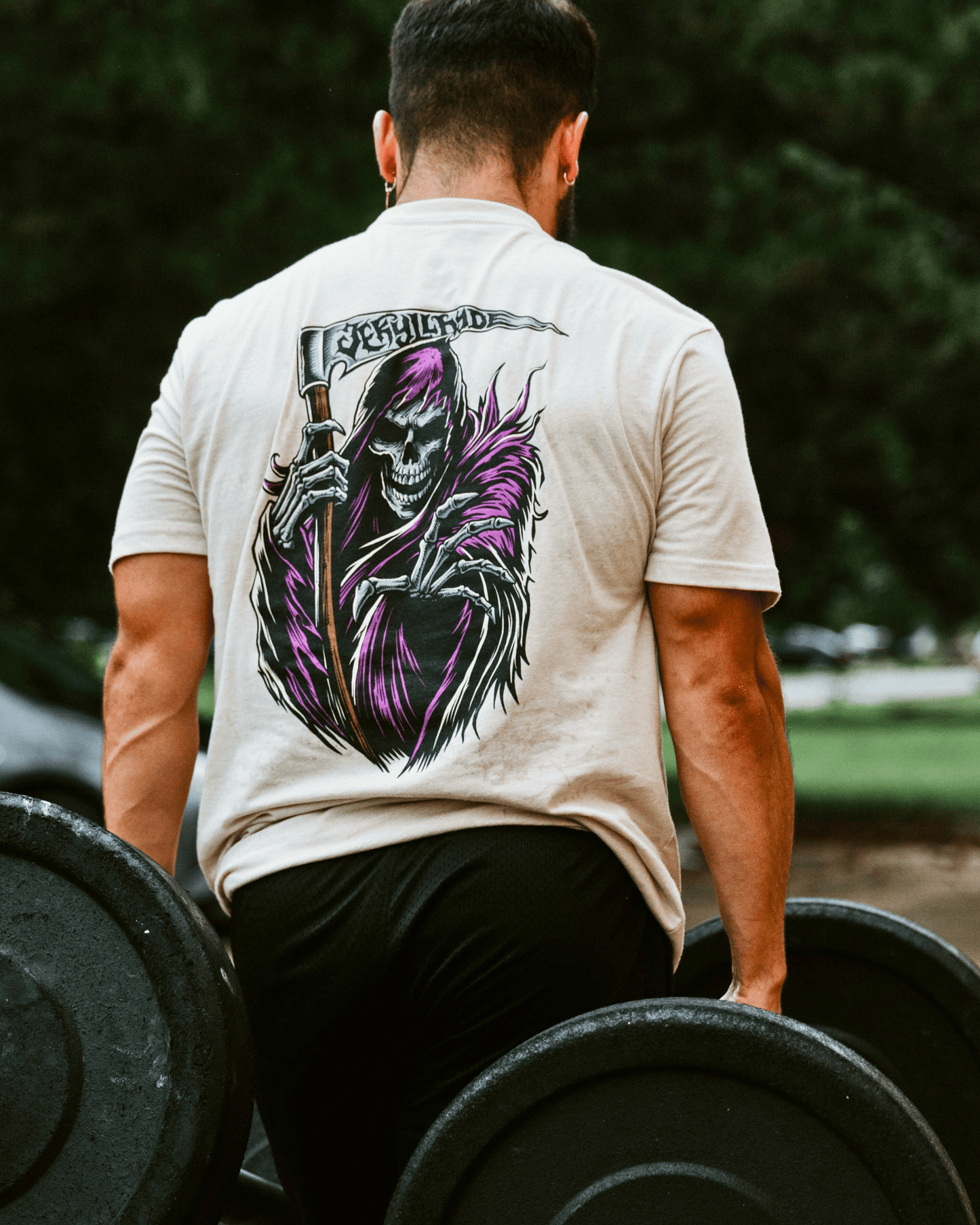 Person lifting weights wearing a t-shirt with a graphic design of a skeleton holding a sword.