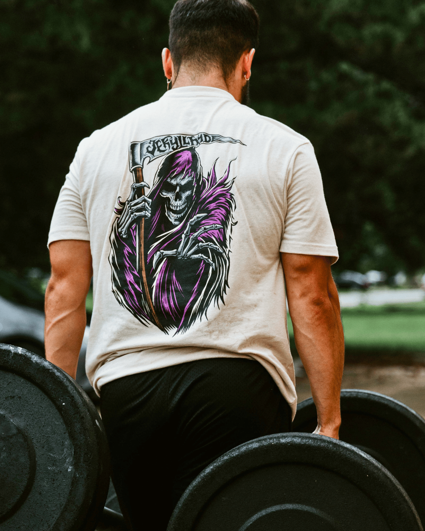 Person lifting weights wearing a t-shirt with a graphic design of a skeleton holding a sword.