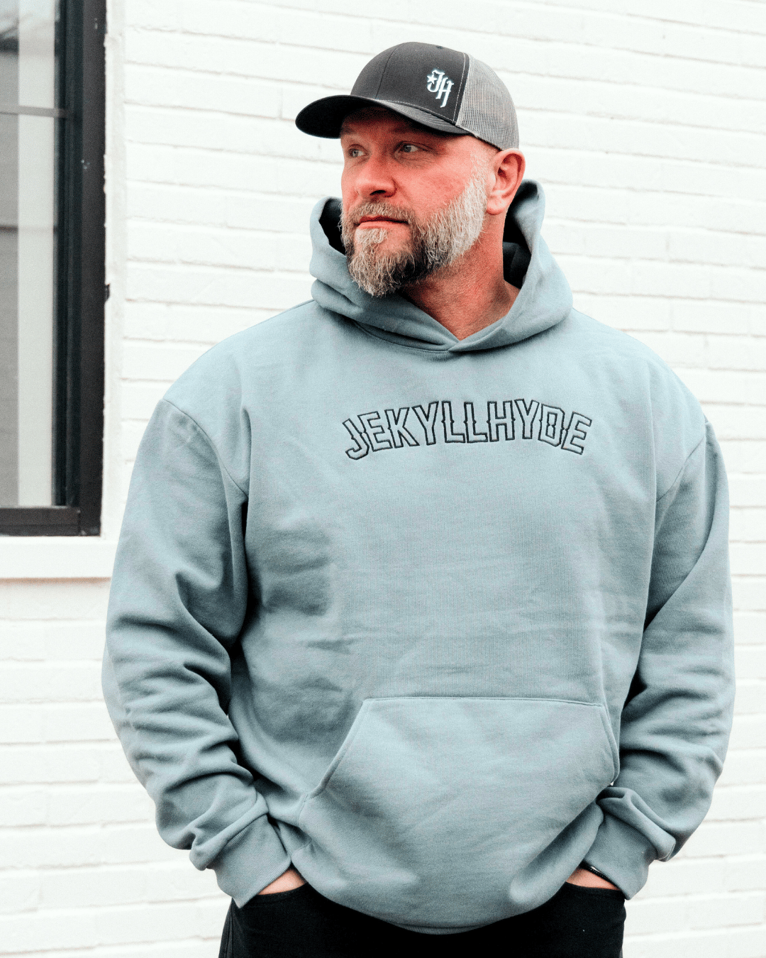 Man standing in a soft blue hoodie against a white brick wall backdrop. 