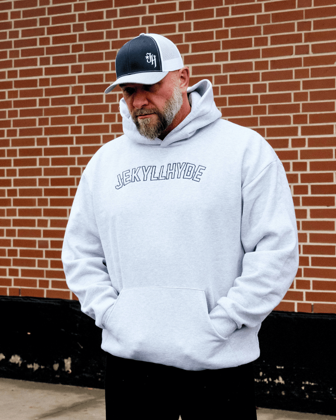 Man standing in a grey hoodie against a red brick wall backdrop. 