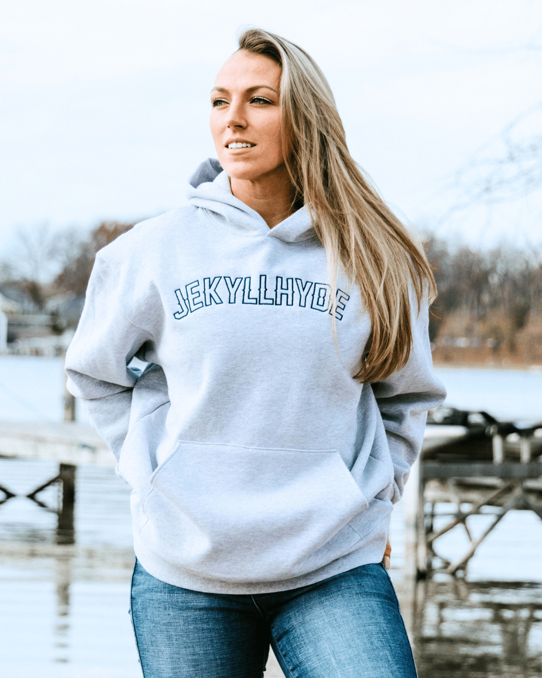 Woman standing on a dock in a grey hoodie. 