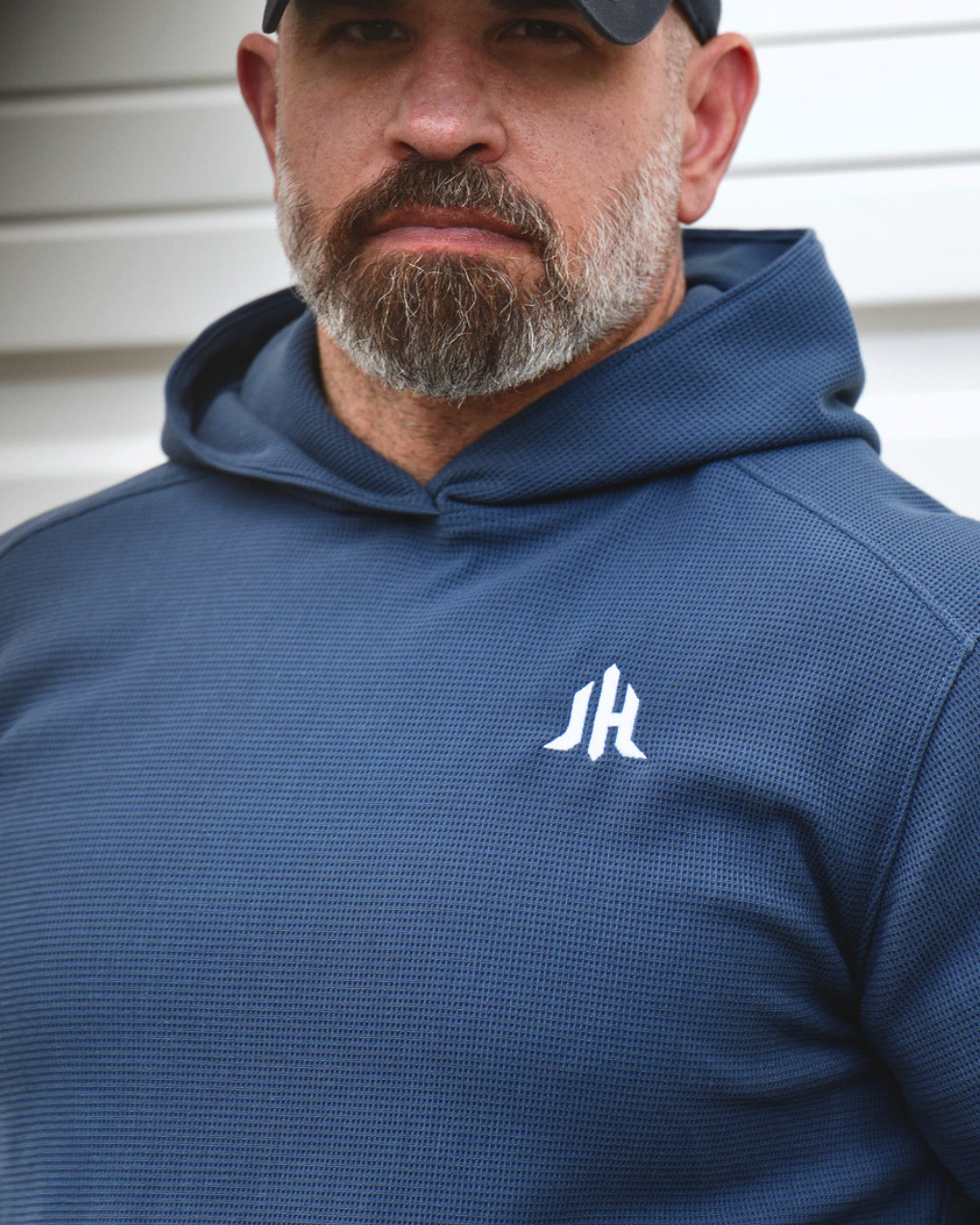 A man wearing a blue waffle knit hoodie with the letters JH embroidered on the left chest. 