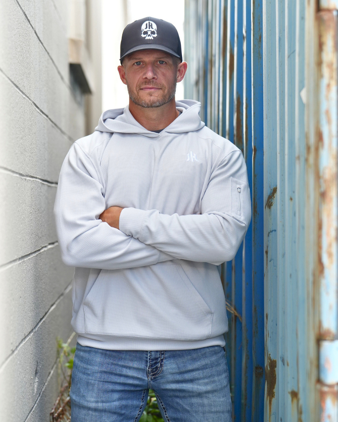 A man standing in between 2 walls wearing a light grey waffle knit hoodie. 