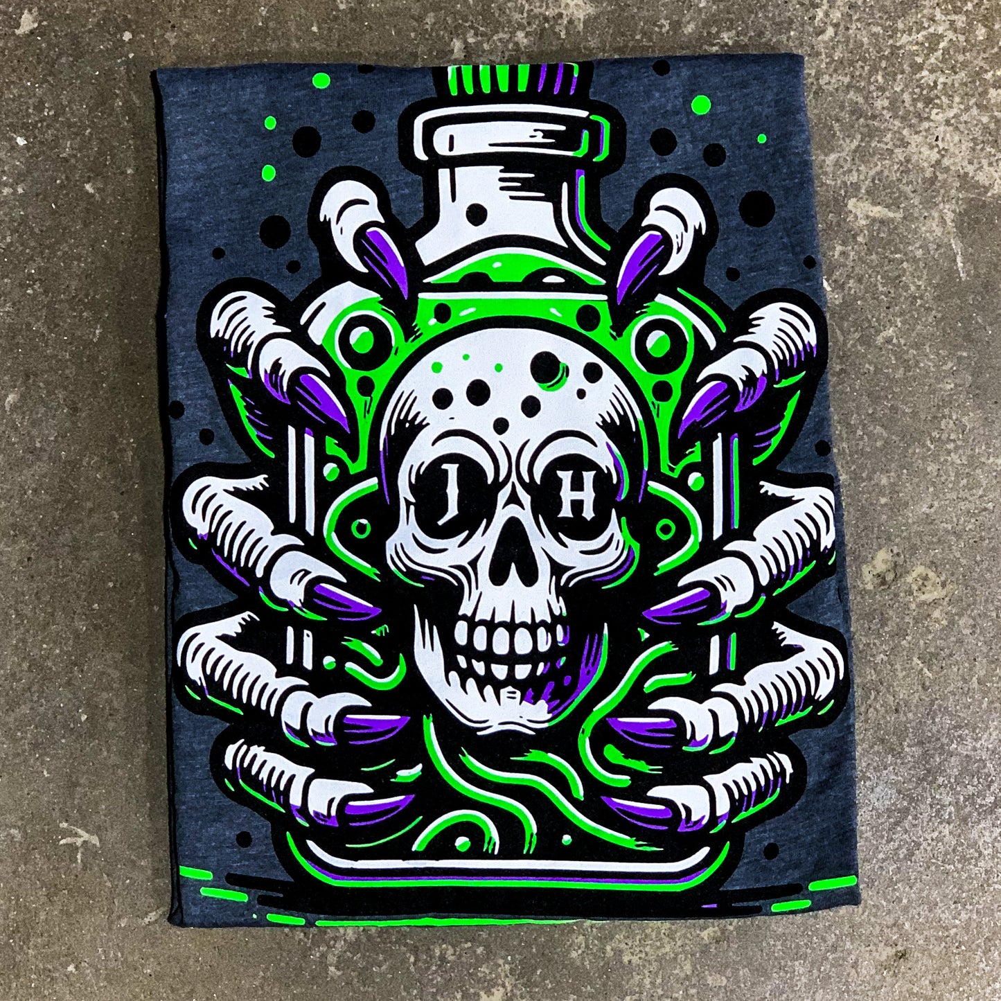 Folded grey shirt on the concrete featuring skulls and claws. 