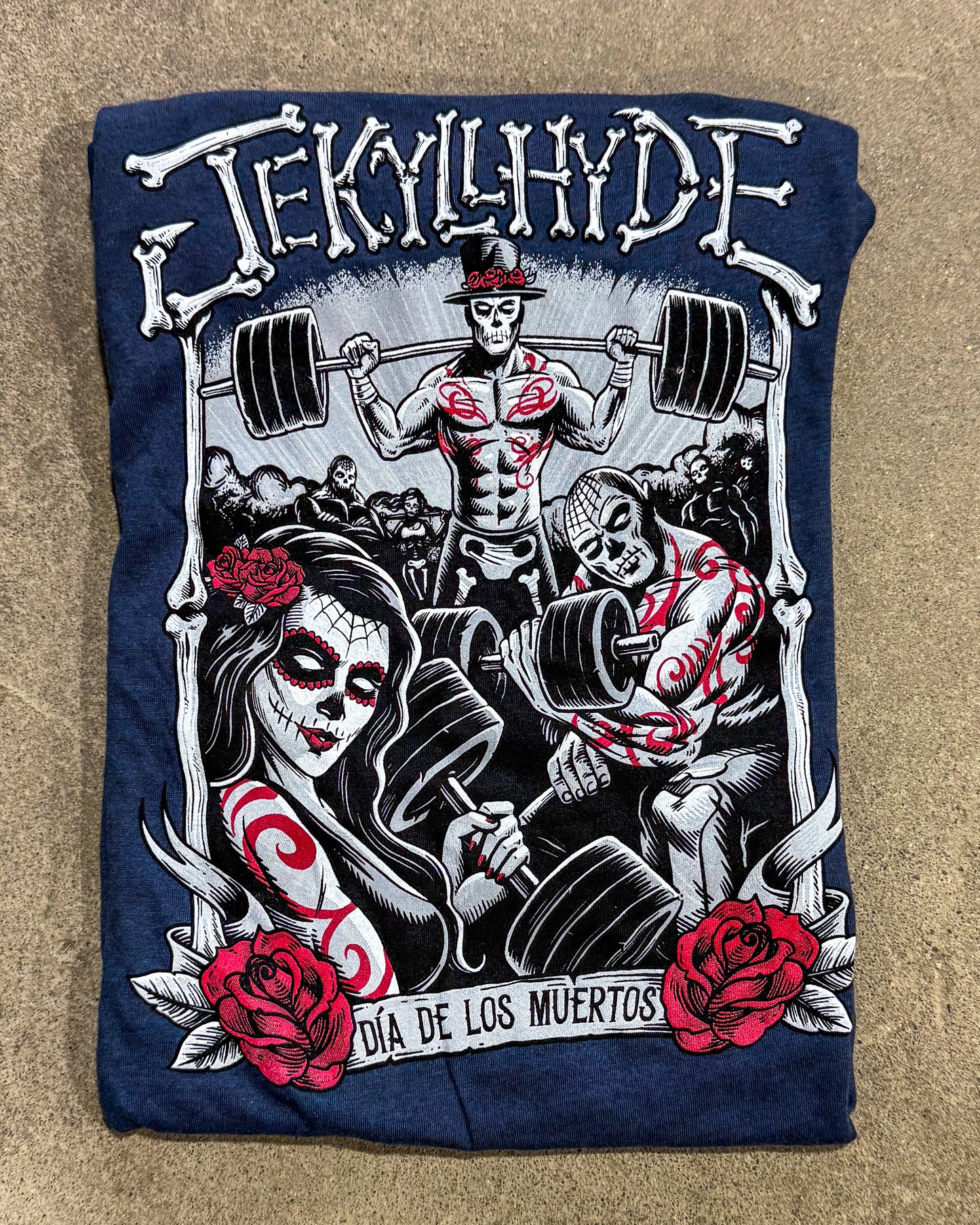 T-shirt with 'Lékyllyhyde' design featuring a skeleton lifting weights, woman with flowers, and roses on a blue background.