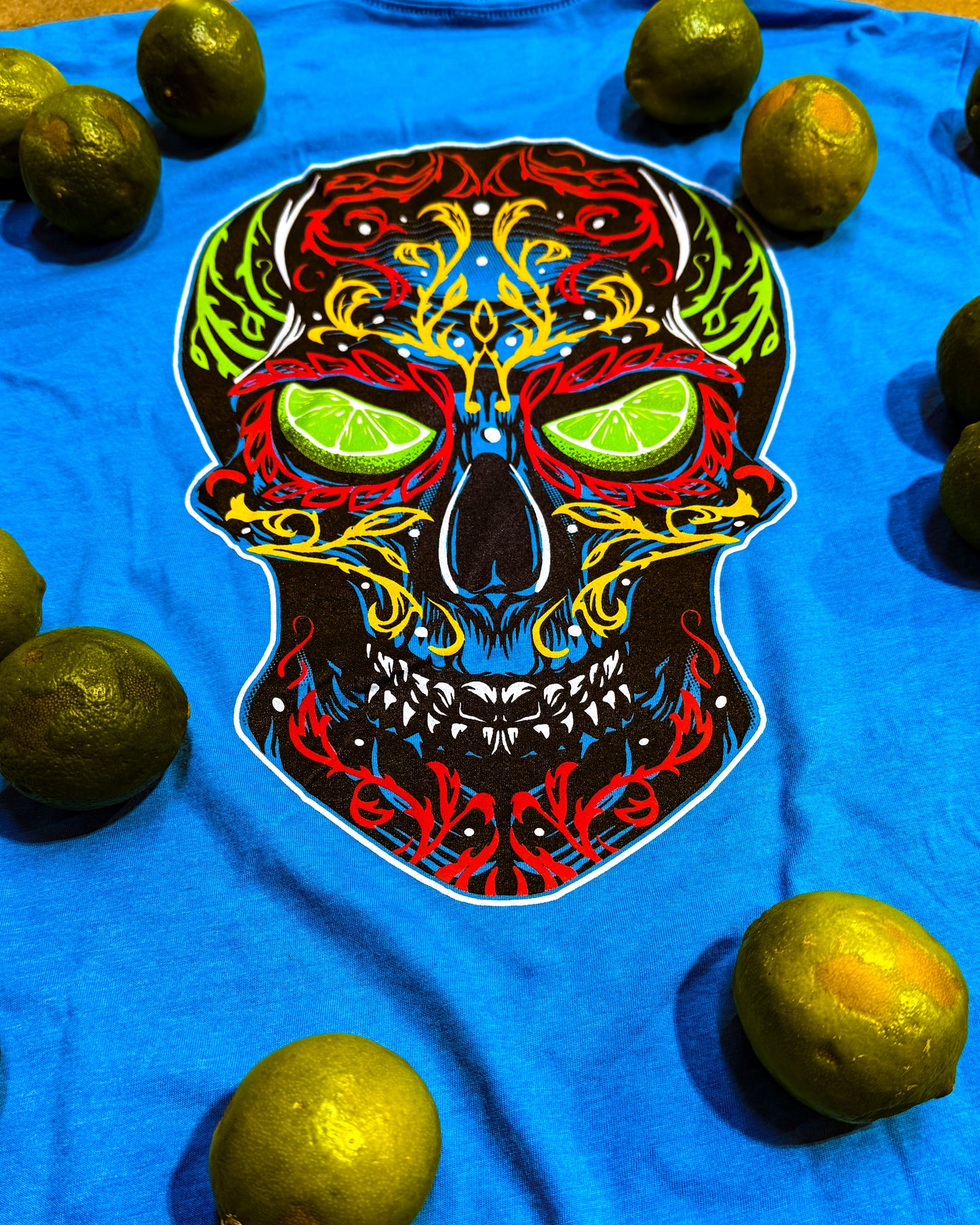 Blue t-shirt with a colorful skull design featuring lime slices for eyes, surrounded by limes.