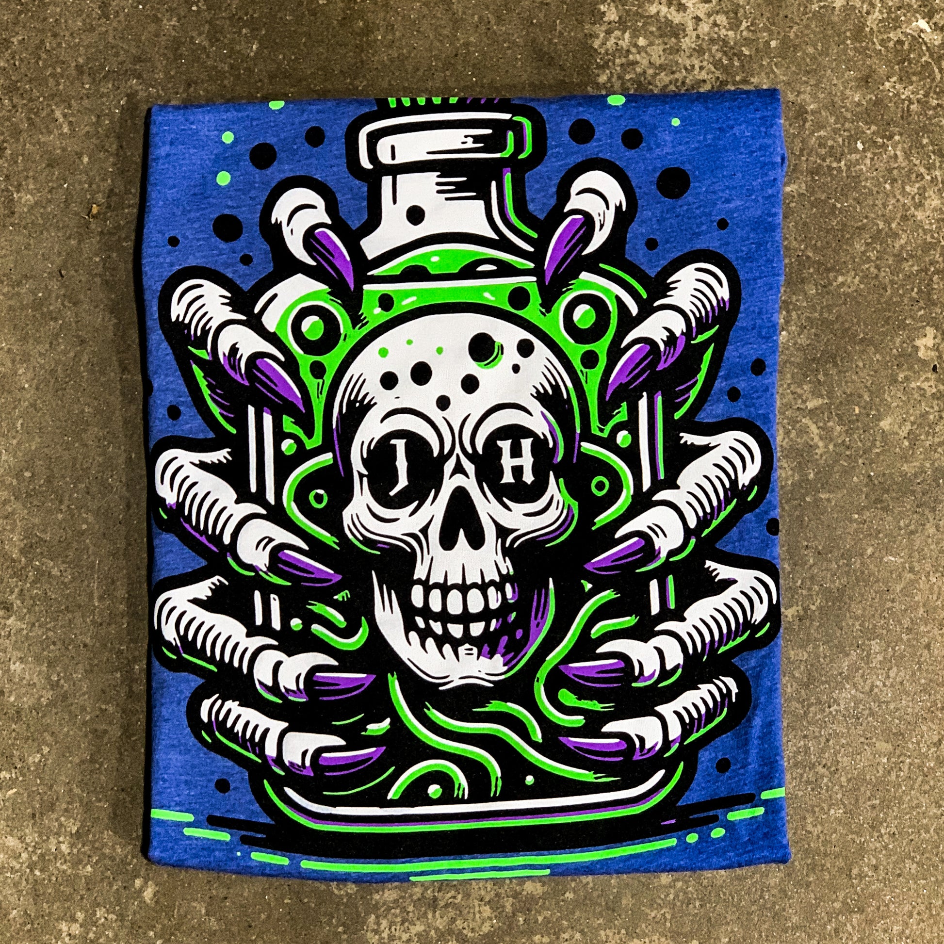 Folded blue shirt on the concrete ground featuring skulls and claws. 