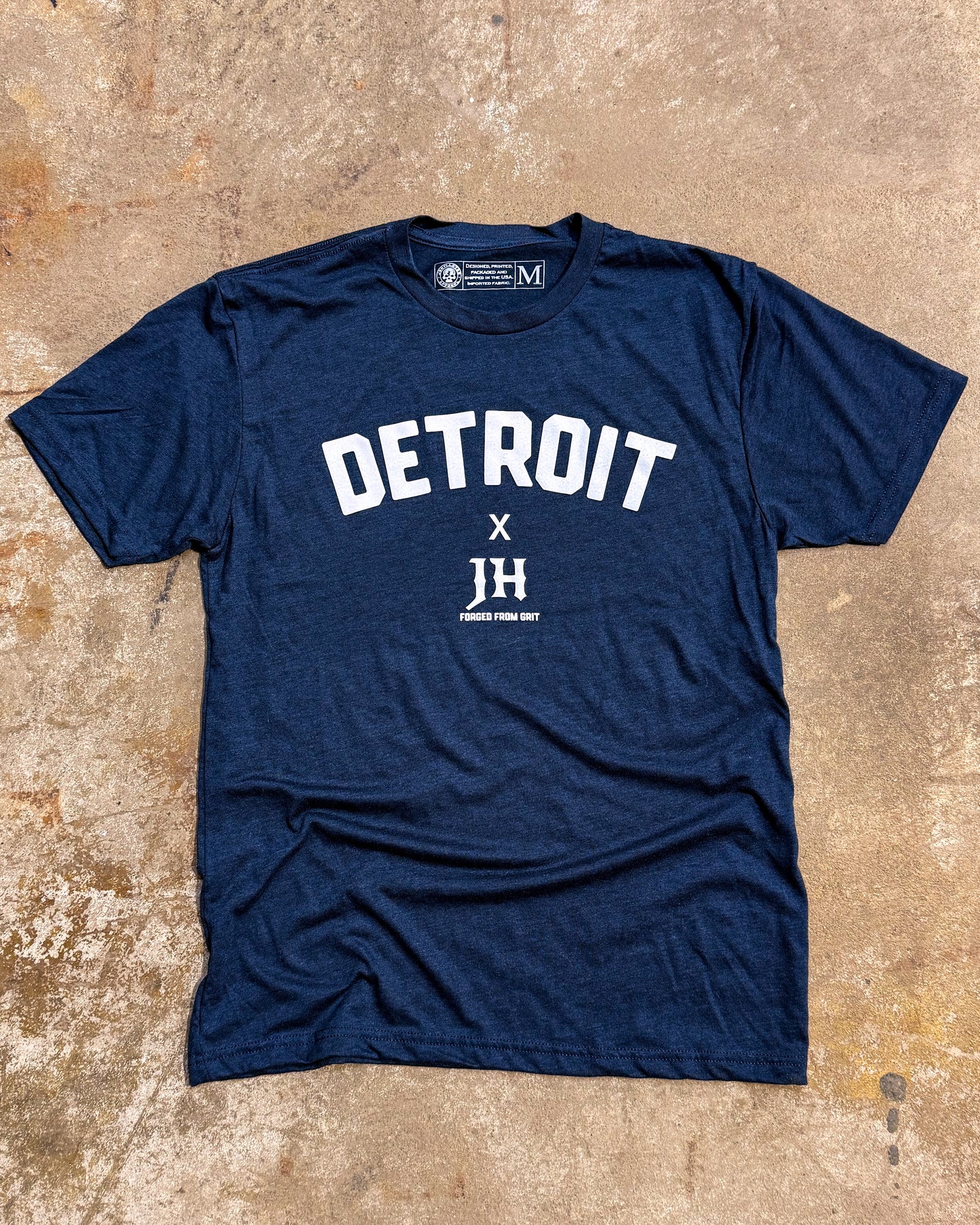 Navy blue t-shirt with 'Detroit' and 'JH' text on a textured beige surface