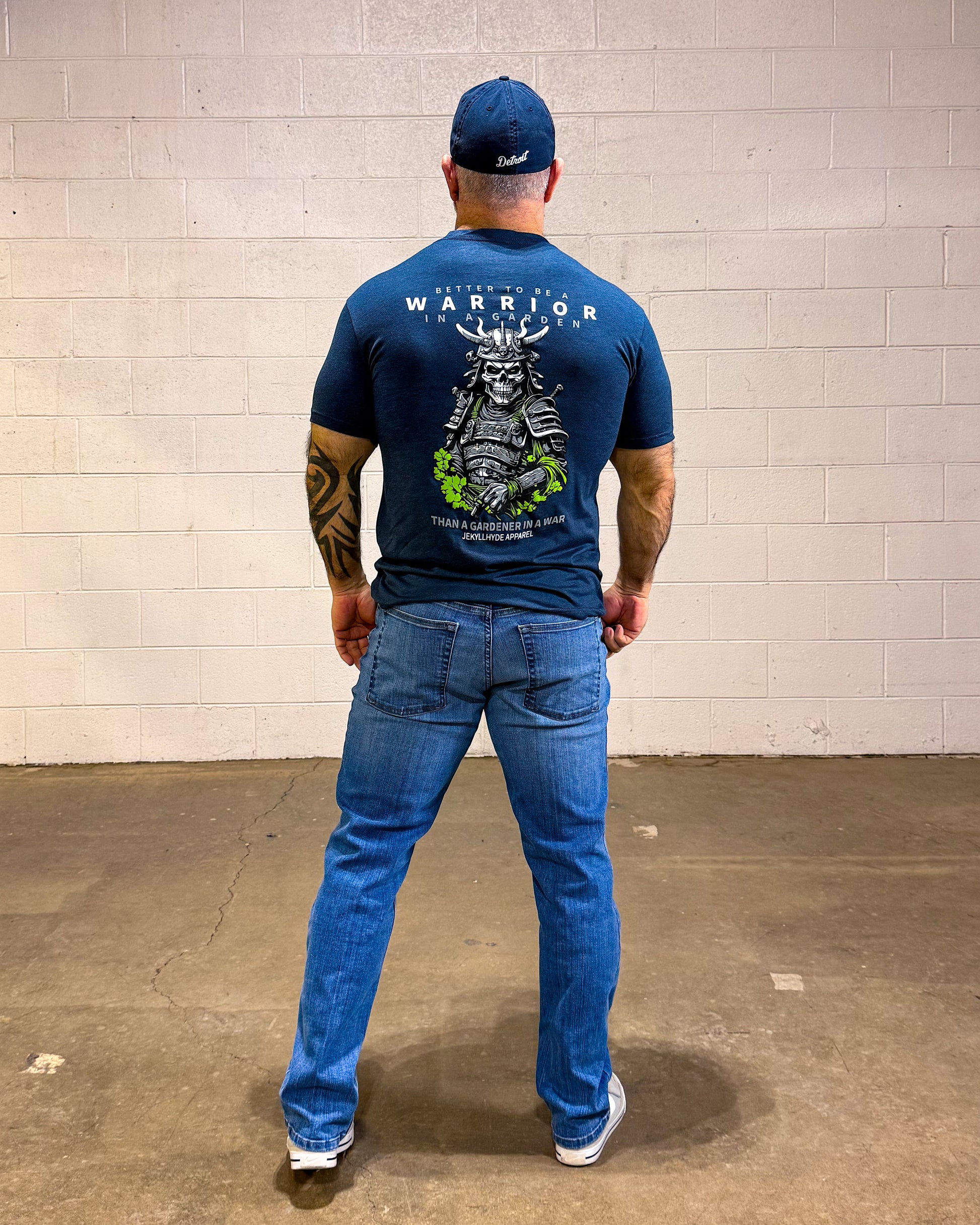Person wearing a blue t-shirt with a graphic design and text, standing against a white brick wall.