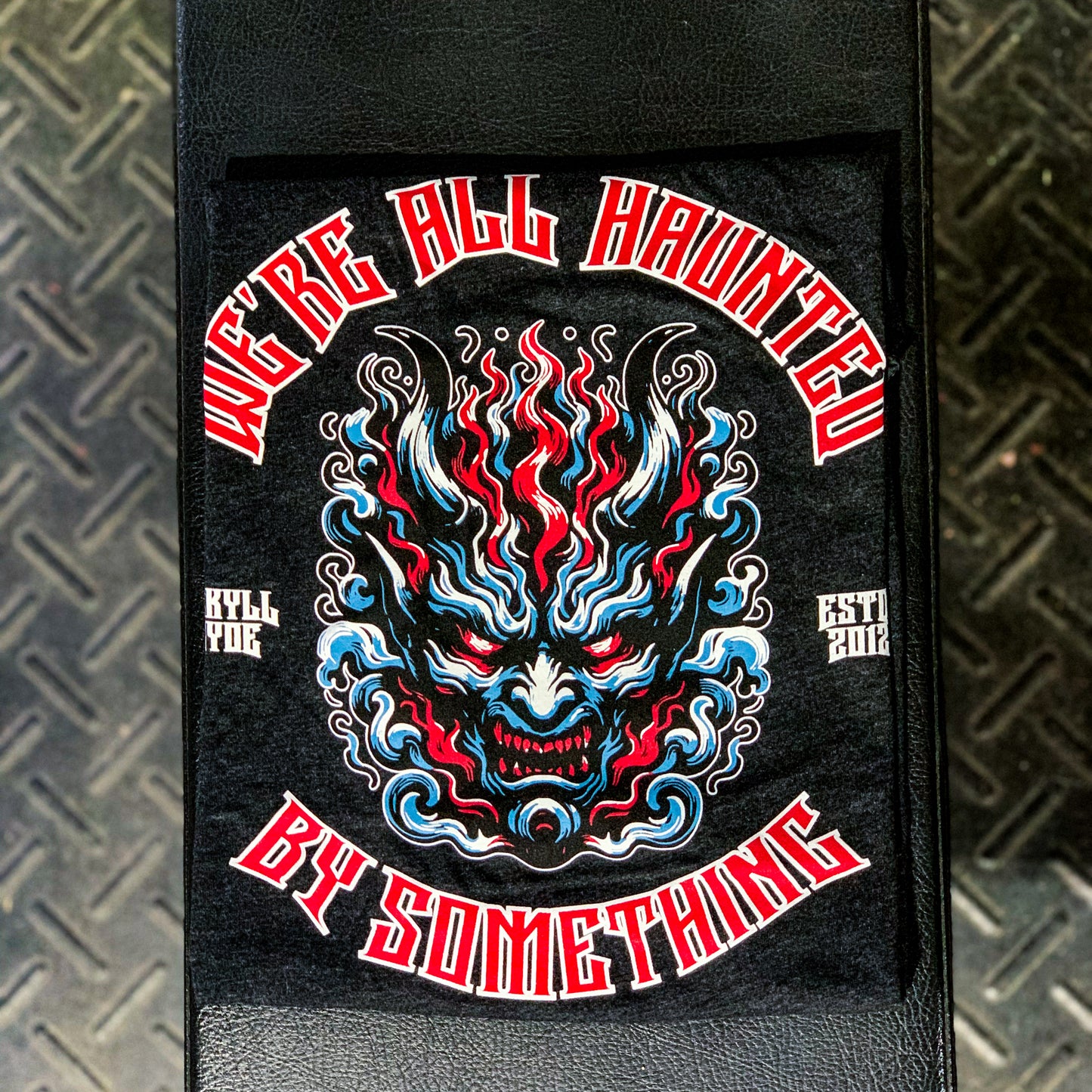 Black tshirt folded on a weight bench with a demon face and text. 