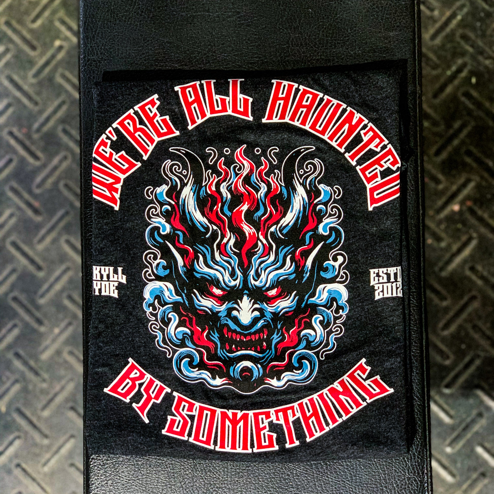 Black tshirt folded on a weight bench with a demon face and text. 