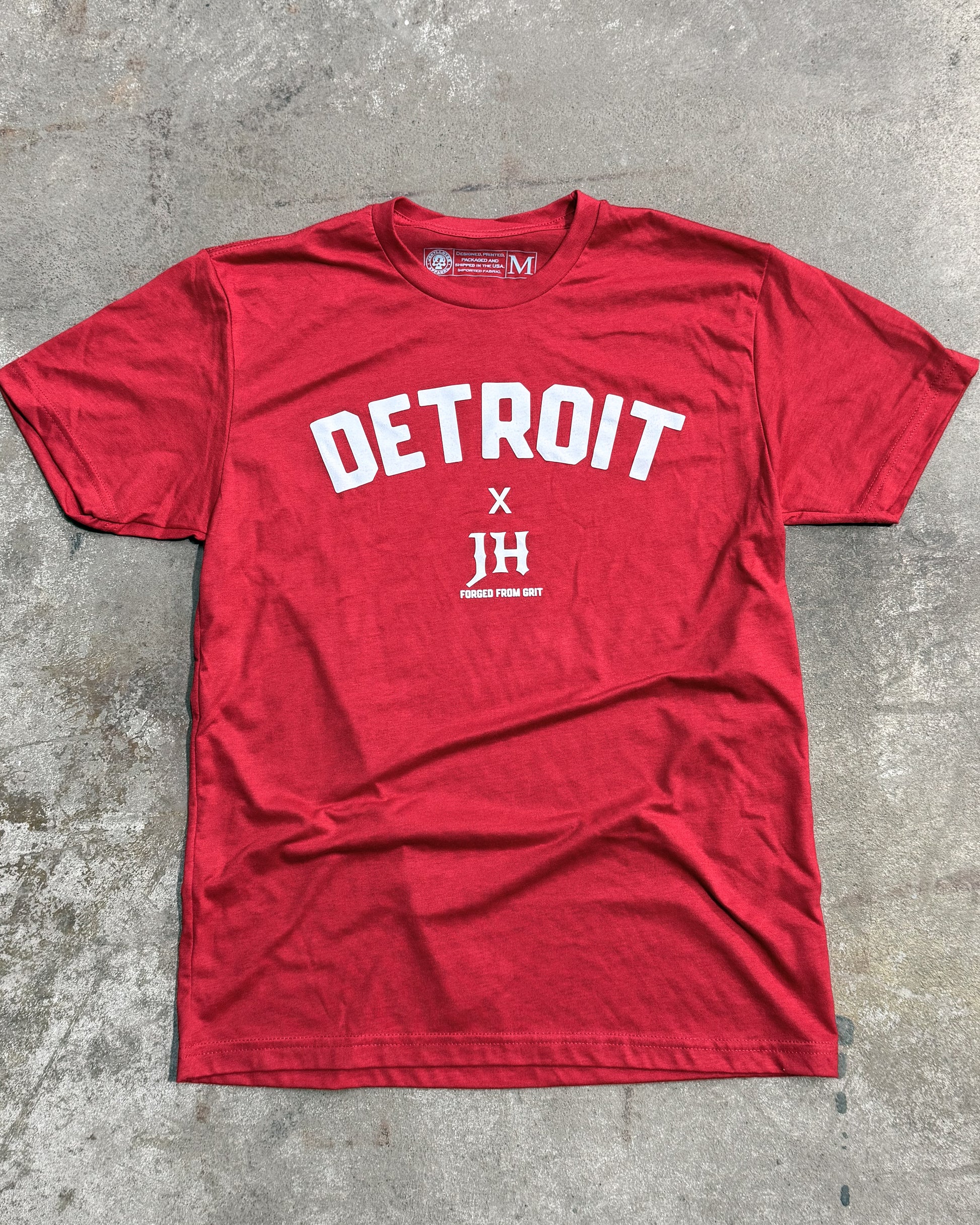 Red t-shirt with 'Detroit X JH' text on a concrete surface