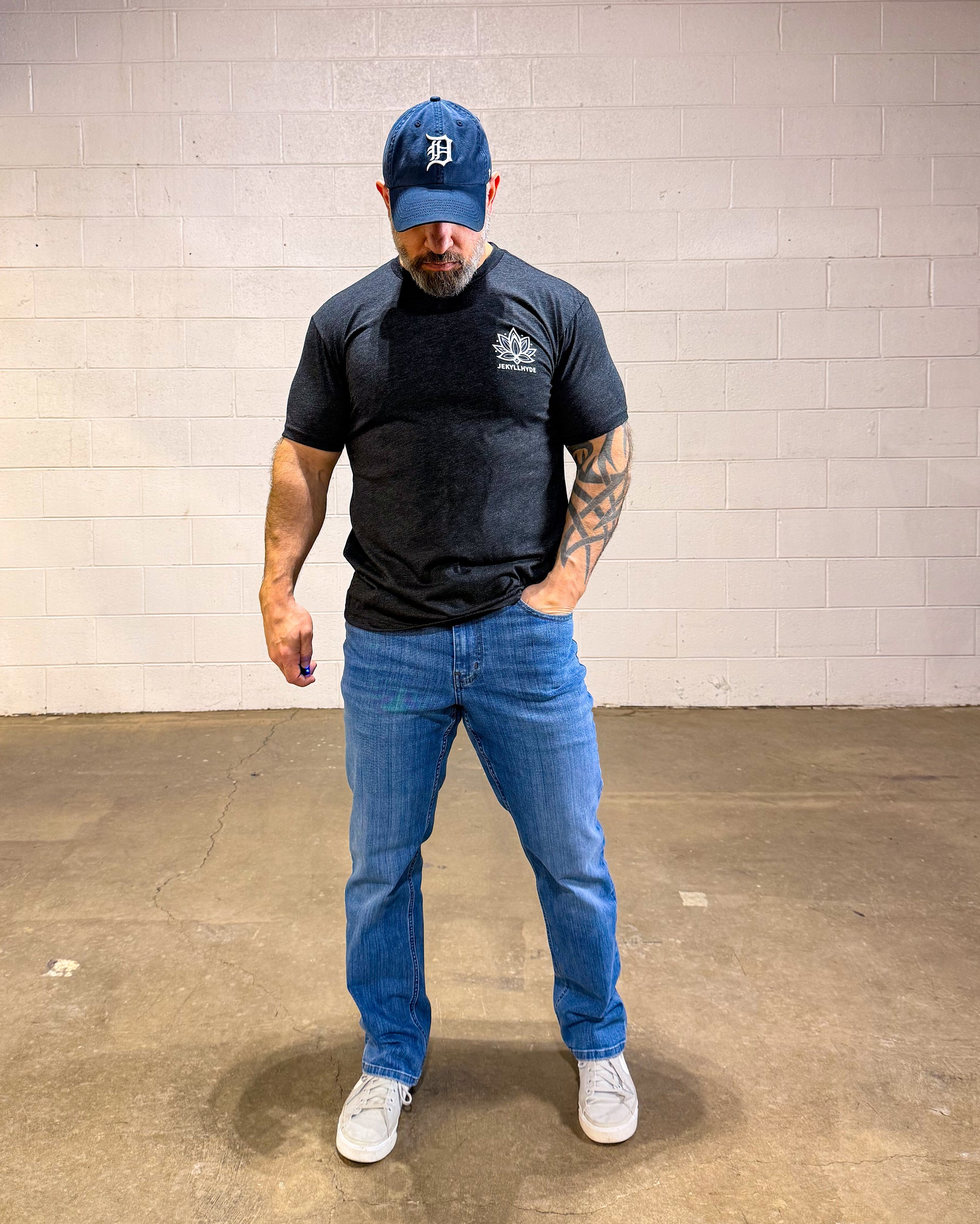 Man wearing a black t-shirt, blue jeans, and a blue cap in an indoor setting.