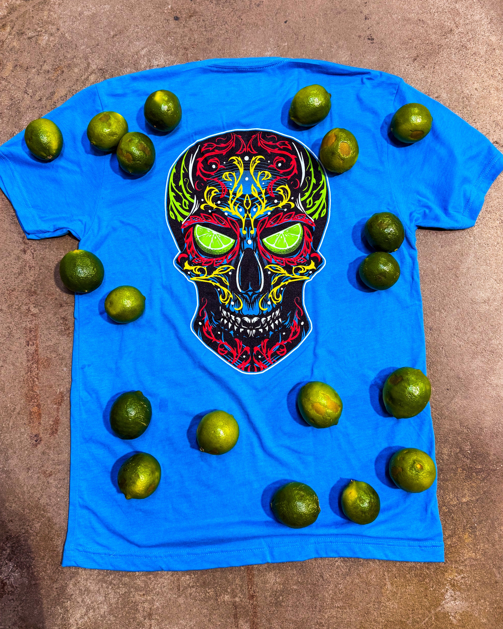 Blue t-shirt with a colorful skull design surrounded by limes on a brown surface