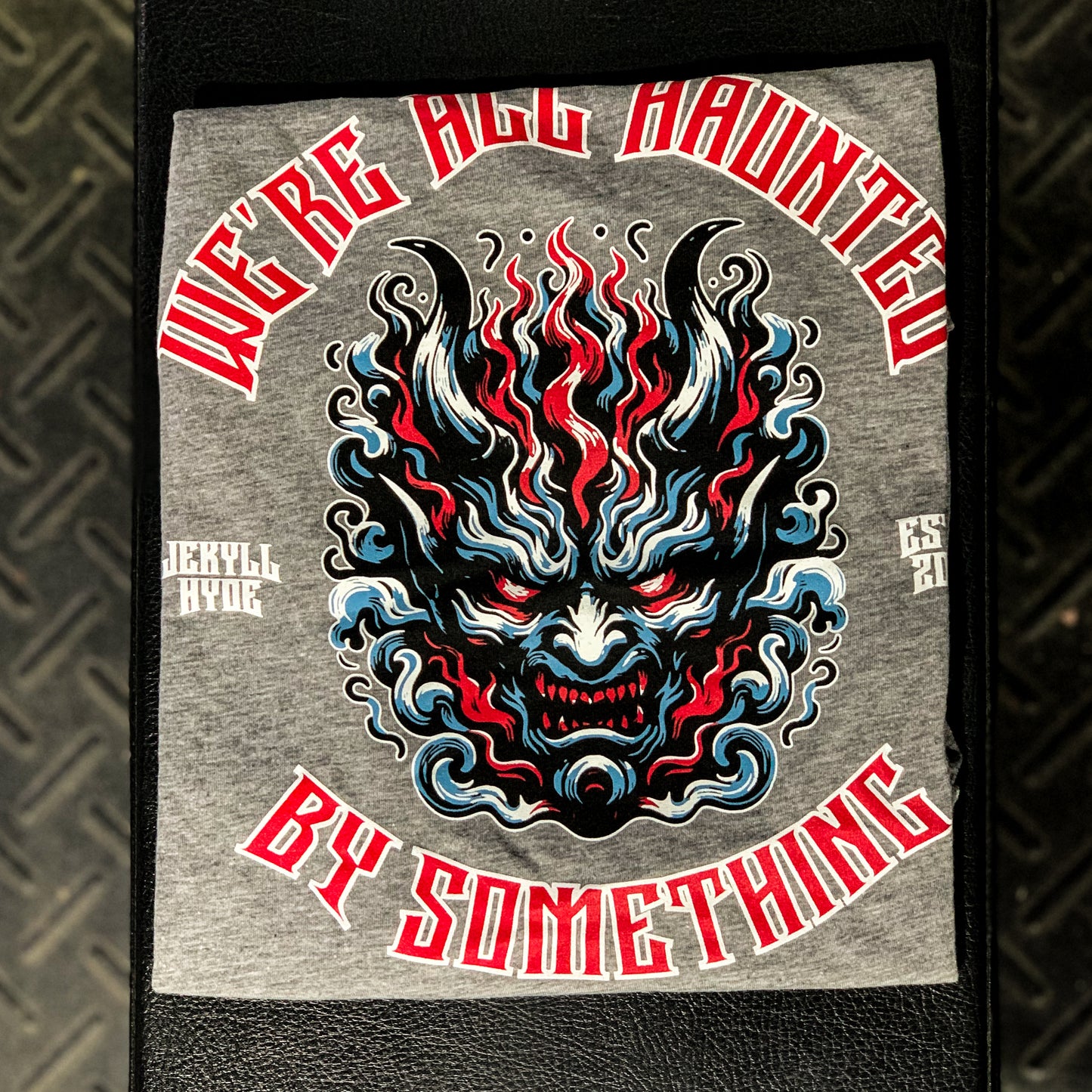 Grey tshirt folded on a weight bench with a demon face and text. 
