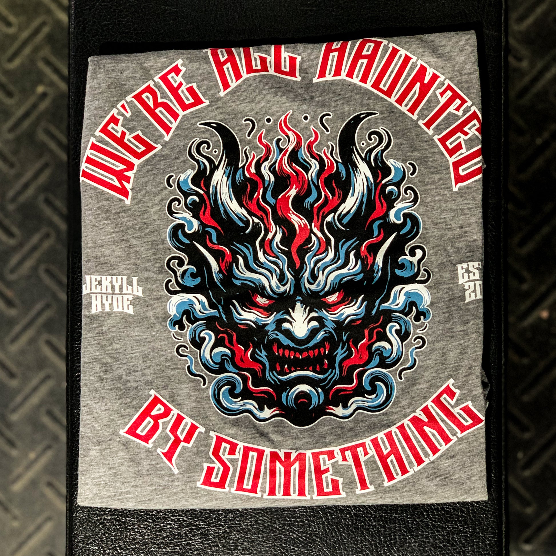 Grey tshirt folded on a weight bench with a demon face and text. 