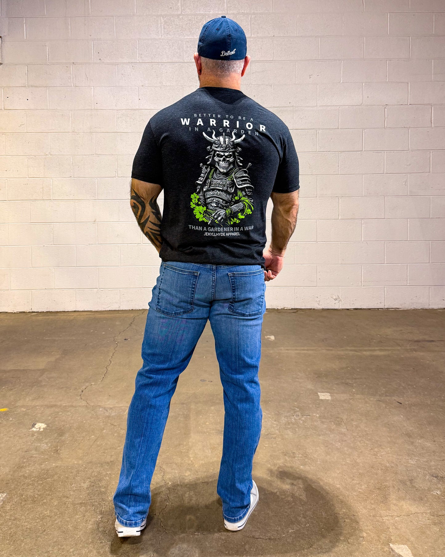 Man wearing a black t-shirt with a graphic design, blue jeans, and a blue cap in an indoor setting.