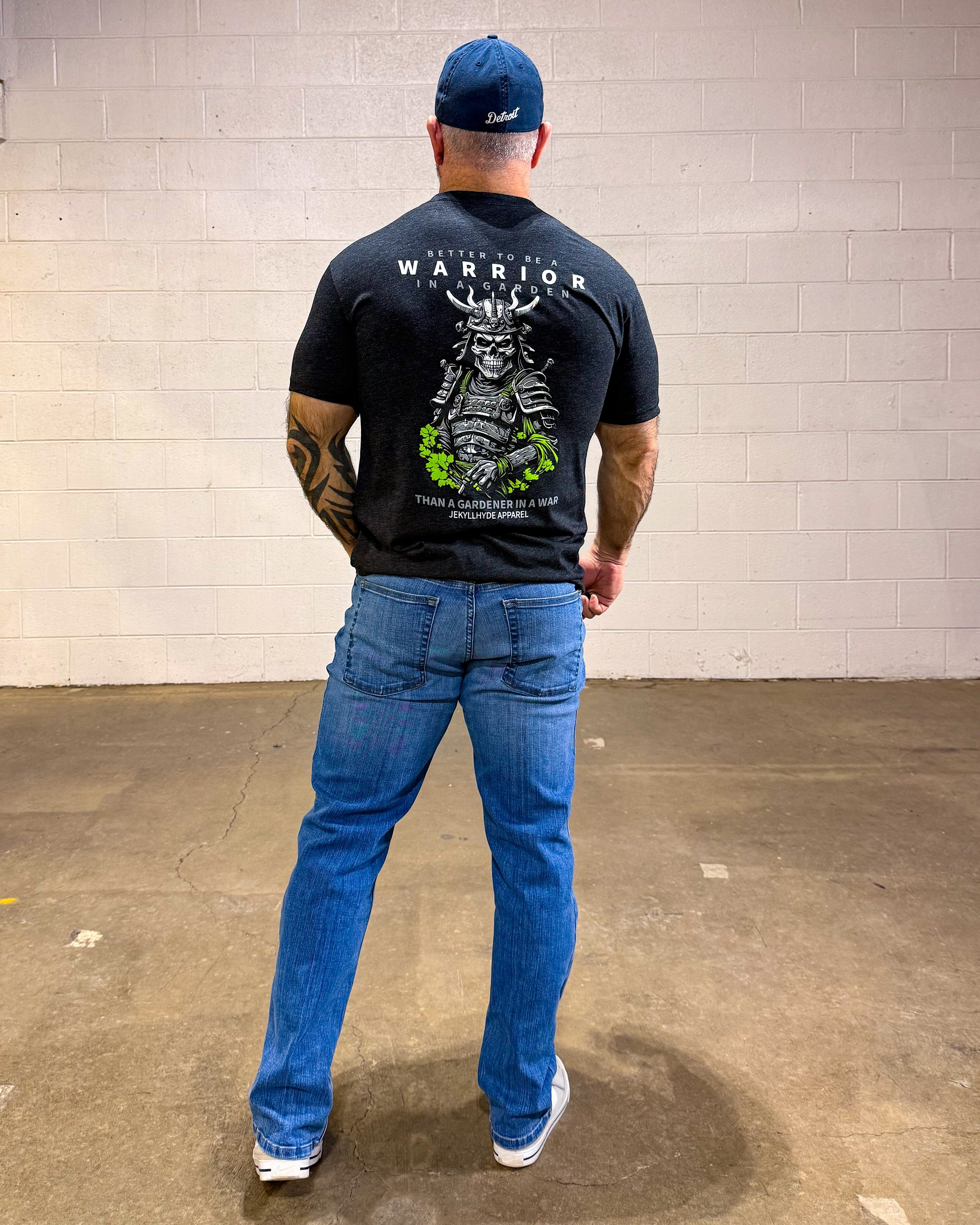 Man wearing a black t-shirt with a graphic design, blue jeans, and a blue cap in an indoor setting.