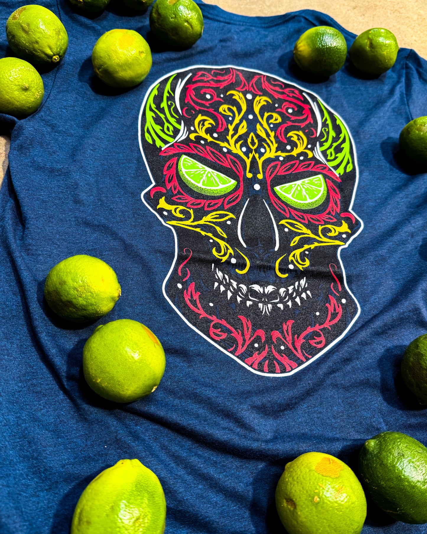 Blue t-shirt with a colorful skull design surrounded by limes on a wooden surface