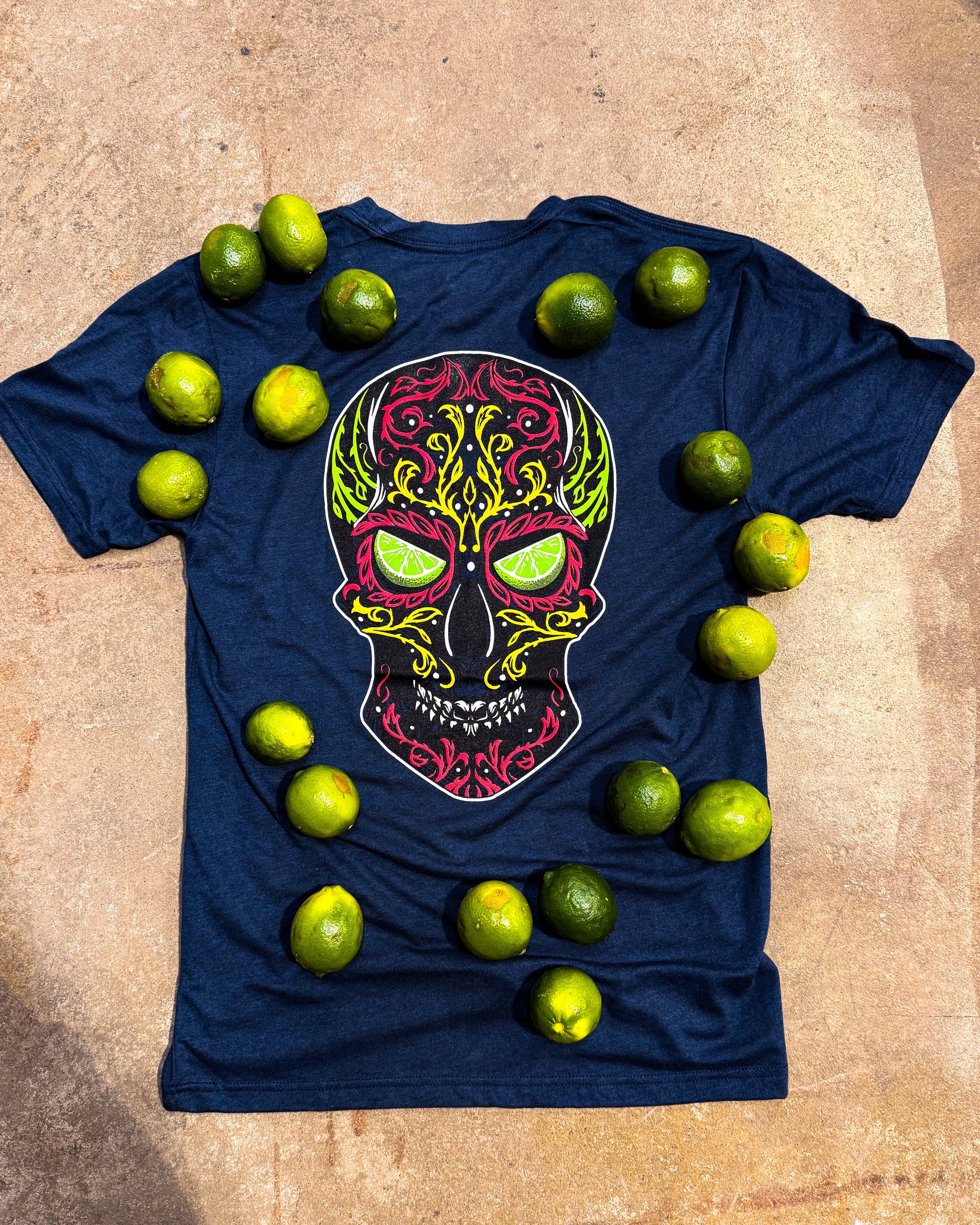 Navy blue t-shirt with a colorful skull design surrounded by limes on a beige surface