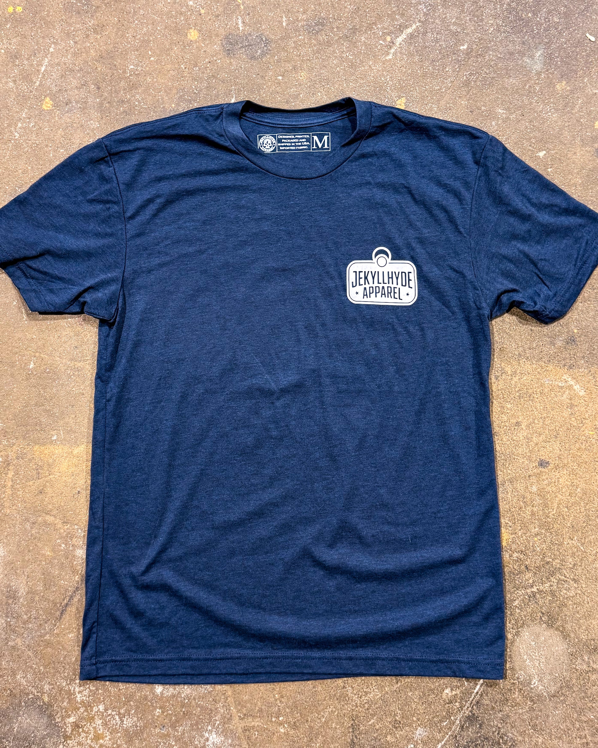 Navy blue t-shirt with a logo on the chest, laid flat on a textured surface.