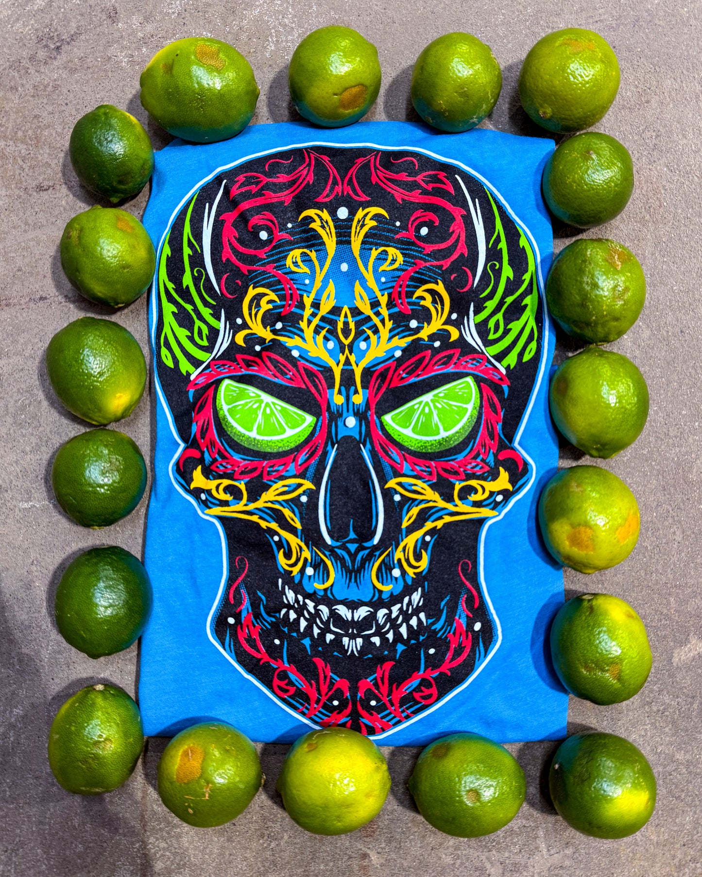 Colorful skull design with lime slices surrounded by limes on a concrete surface