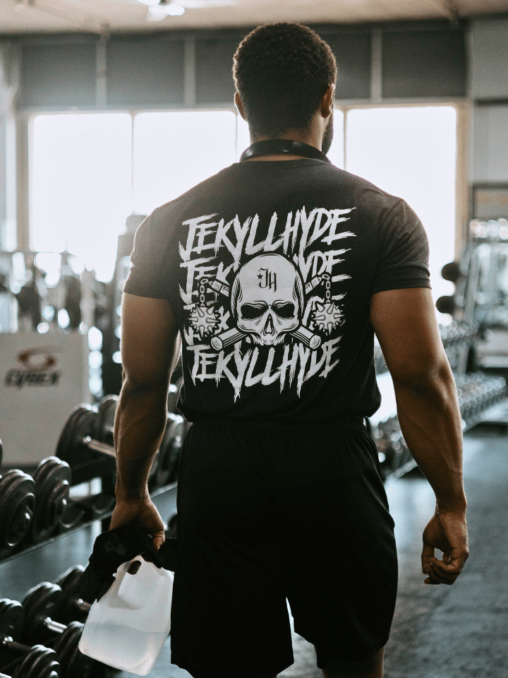 Man walking in front of dumbbell rack wearing a black shirt with a skull and mace on it. 