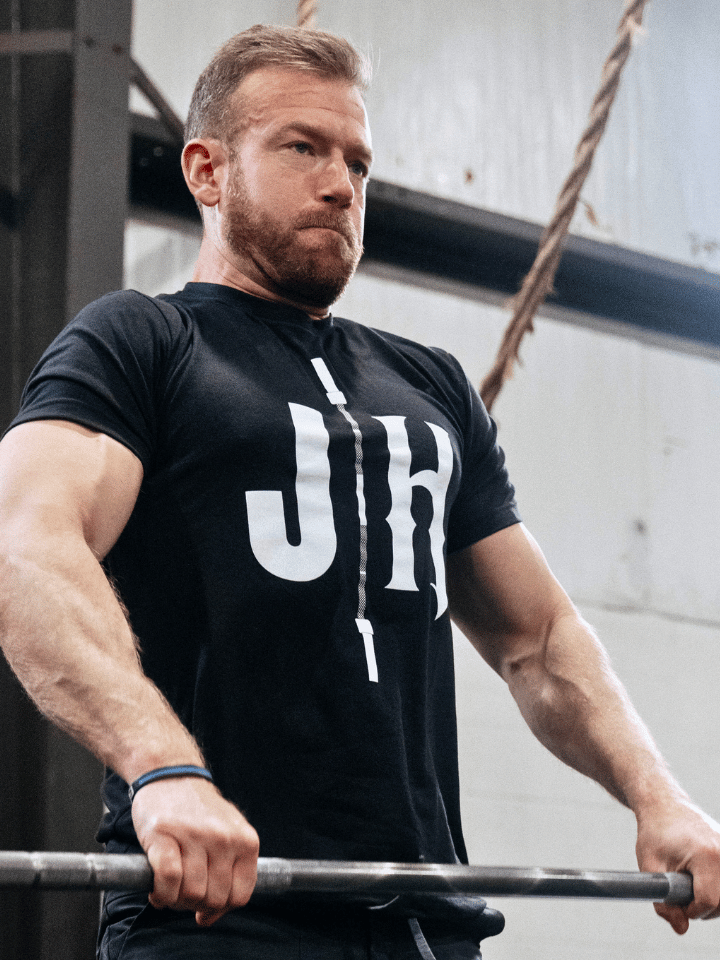 Man lifting a barbell in a black shirt with a JH on the front. 