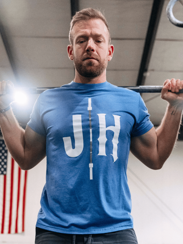 Man squatting a barbell wearing a blue shirt with a barbell and JH on it. 