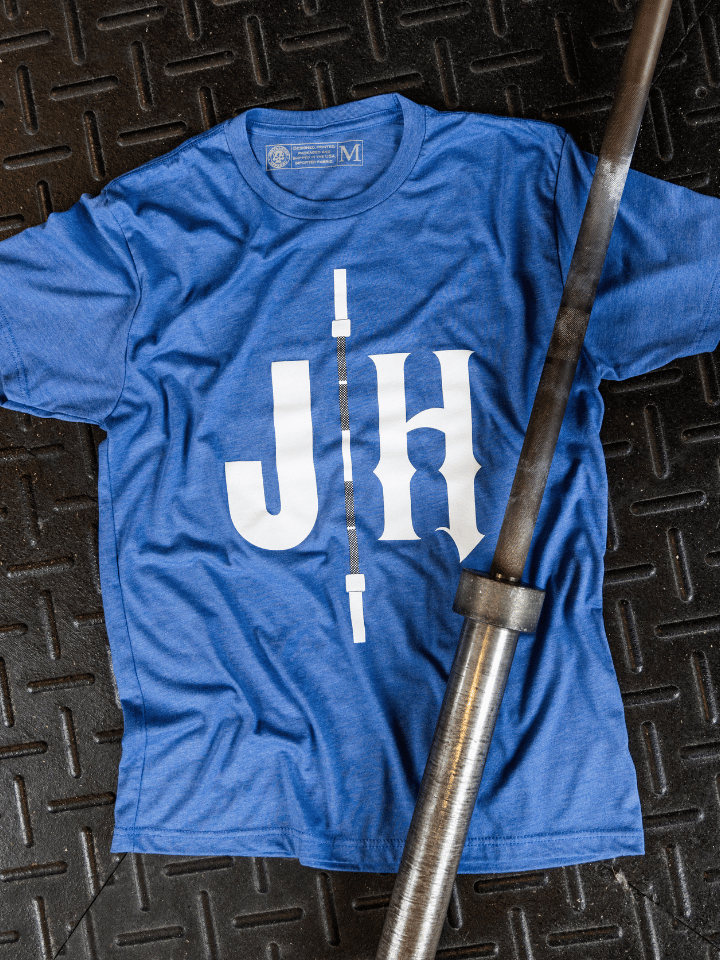Blue shirt laying on the ground with a barbell across it. 